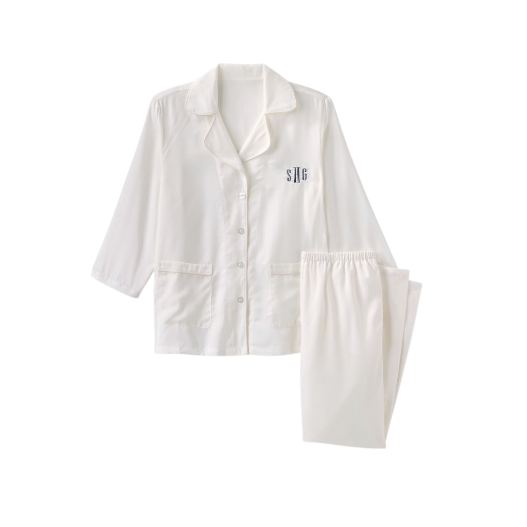 A set of white sateen long-sleeve pajamas with a subtle monogram embroidered on the chest pocket.