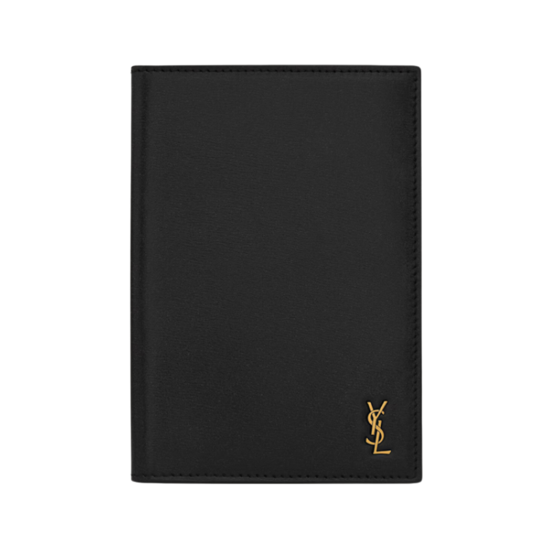 A black textured-leather Yves Saint Laurent passport holder featuring a gold YSL metal monogram in the corner.