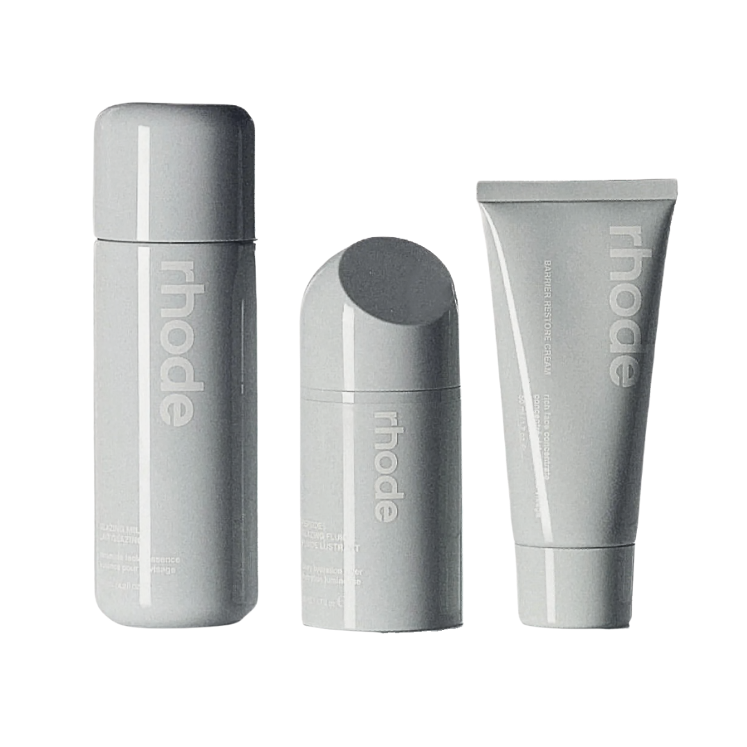 A trio of Rhodes skincare products in minimalist grey packaging, including a fluid, a cream, and a lip treatment.