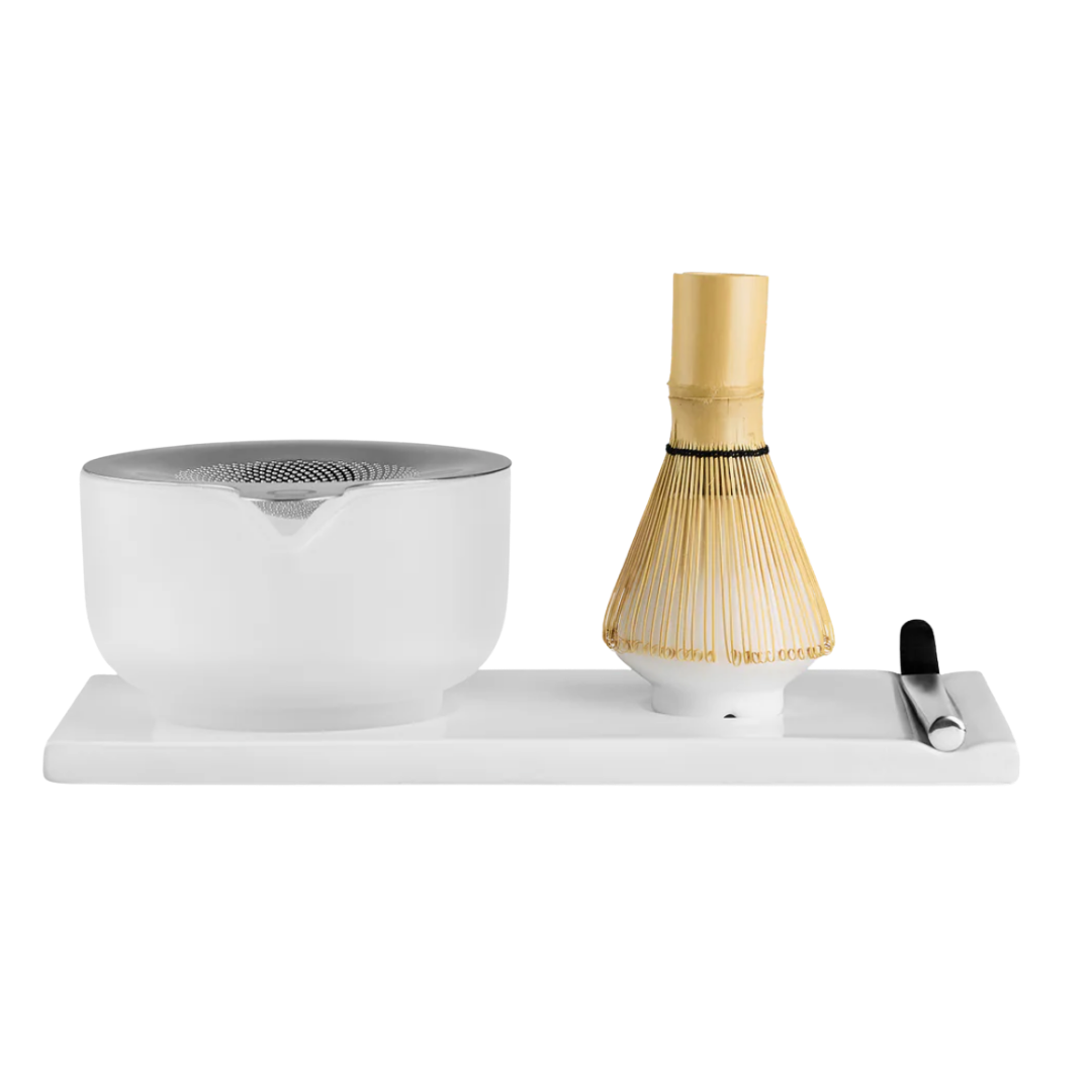 Modern minimalist ceremonial matcha tea brewing set with white ceramic bowl, bamboo chasen whisk, and scoop on matching tray