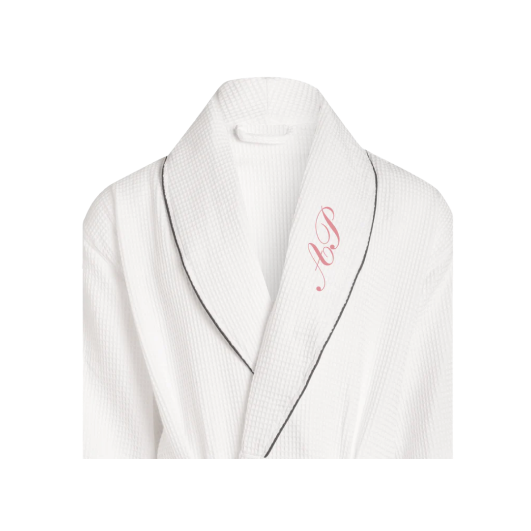 A luxury white waffle-knit cotton bathrobe featuring black piping and a personalized red monogram on the lapel.