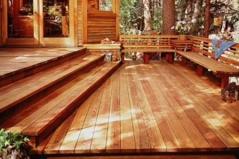 Terraza exterior de madera con escalones y un banco empotrado rodeada de árboles.