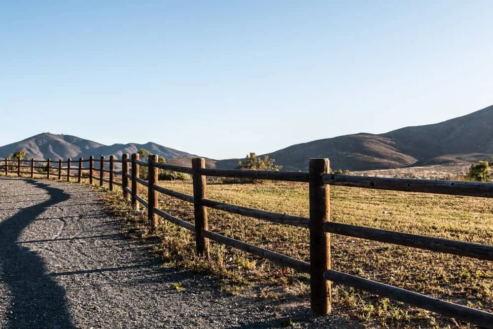 Dirt road and wooden fence with mountains in the background.
