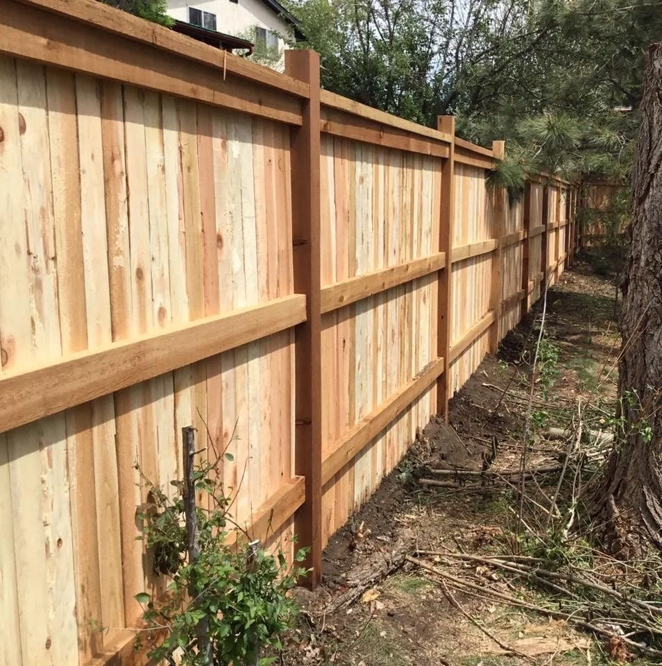 Wooden privacy fence along a yard with shrubs and trees nearby