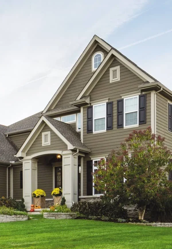 Suburban house with a gable roof, light brown siding, black shutters, and a manicured lawn