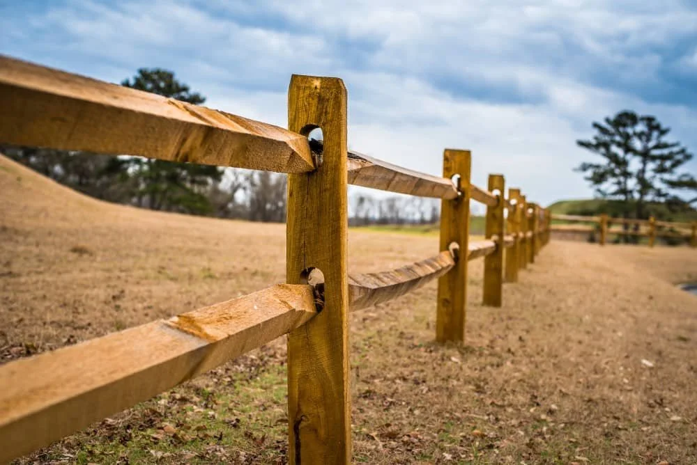 Wooden split rail fence on grassy field under cloudy sky