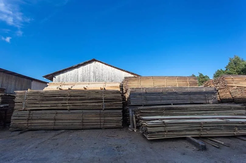 Large stacks of lumber in a lumberyard under a clear blue sky.