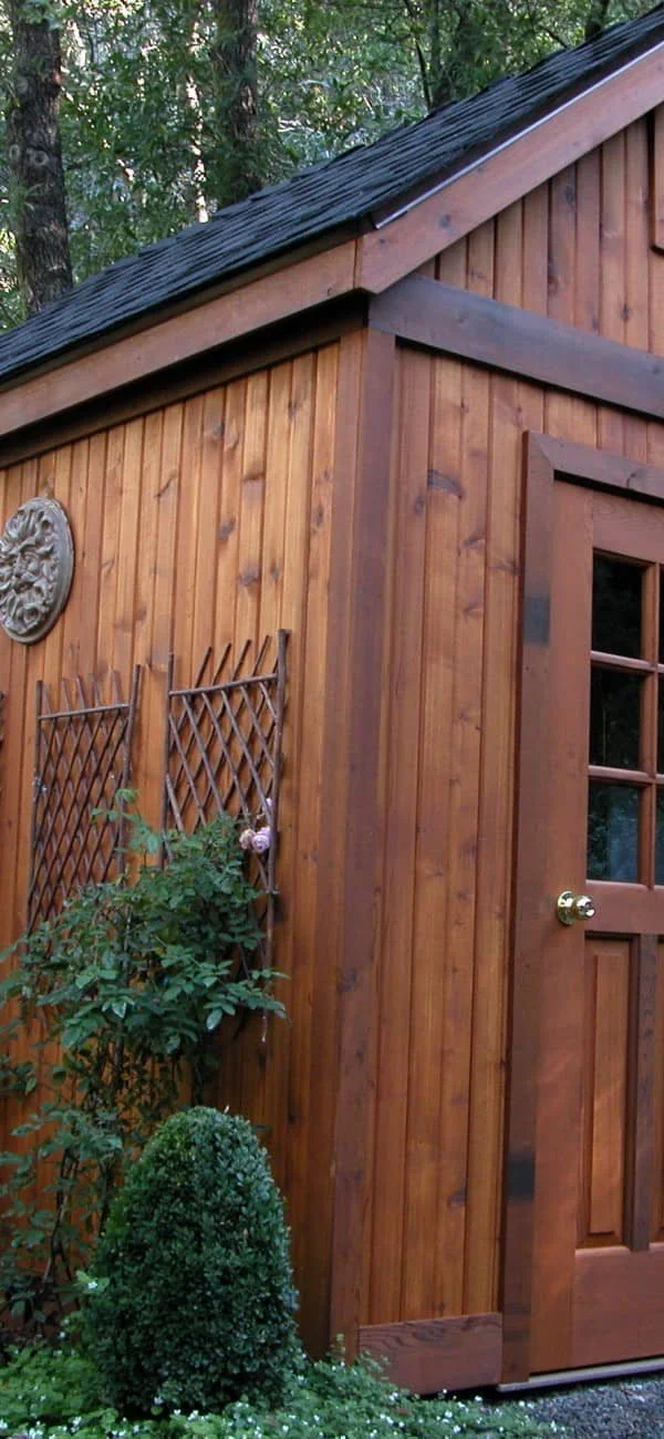 Wooden shed with a door and trellis, surrounded by plants.