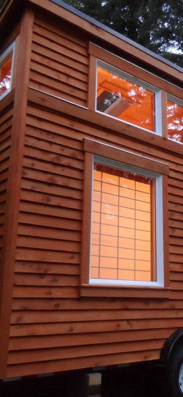 Exterior of a tiny house with wooden siding and large windows.