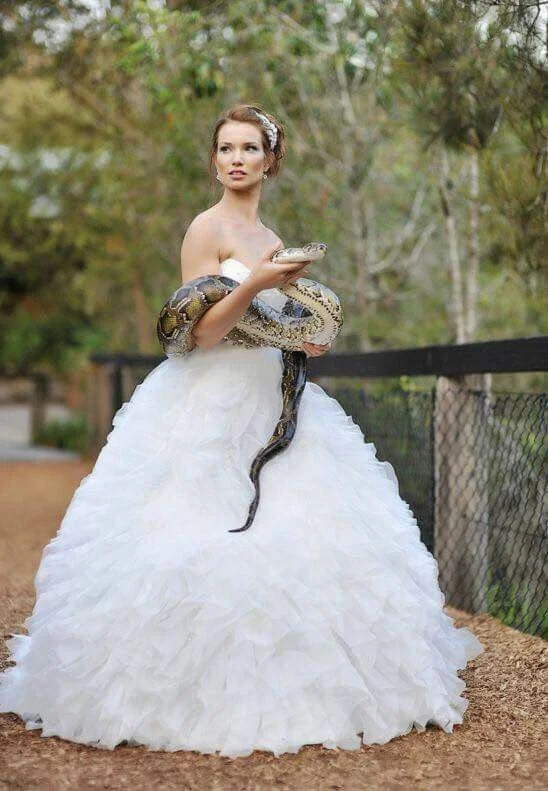 A woman in a white wedding dress standing outdoors holding a snake.