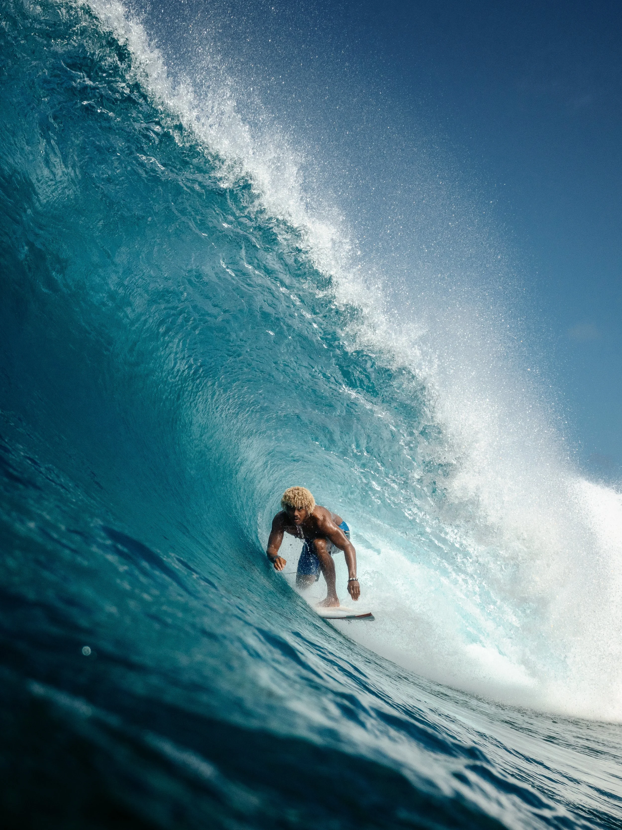 A person with blonde hair surfing inside a large ocean wave.
