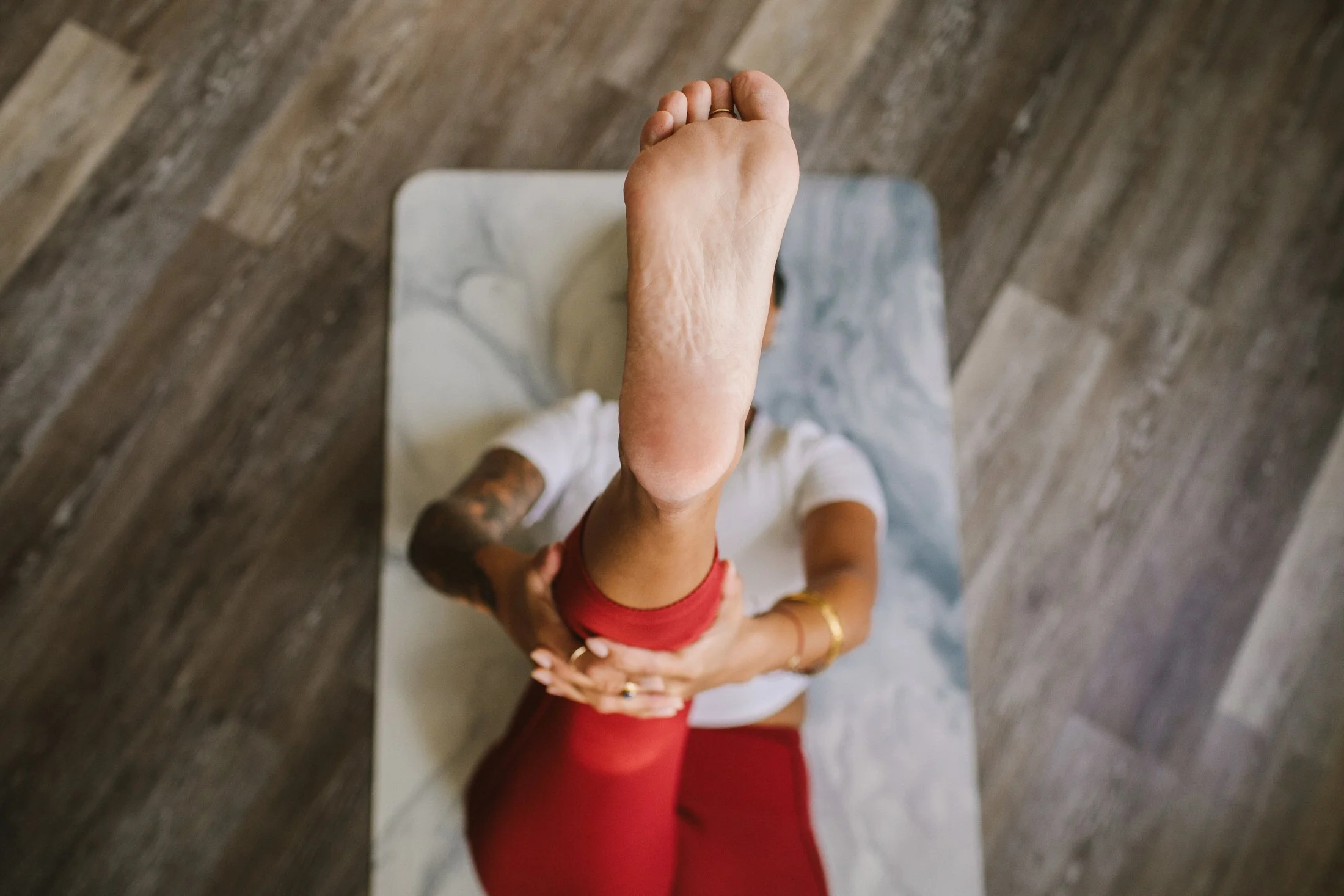 Overhead view of a woman standing on a weighing scale with her hand resting on her stomach, wearing a red sports bra and red pants, standing on a wooden floor.