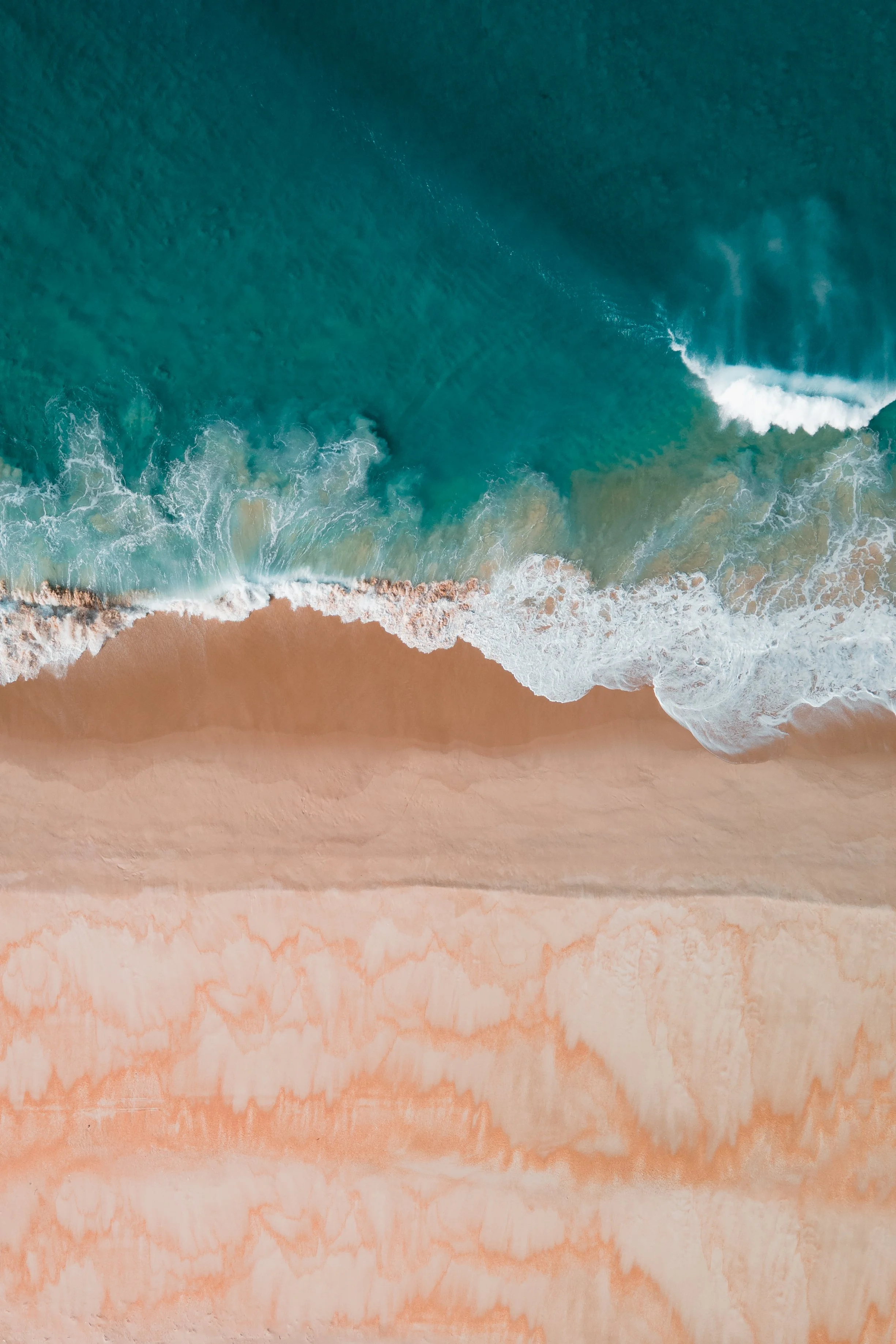 An aerial view of the ocean waves crashing onto a sandy beach.