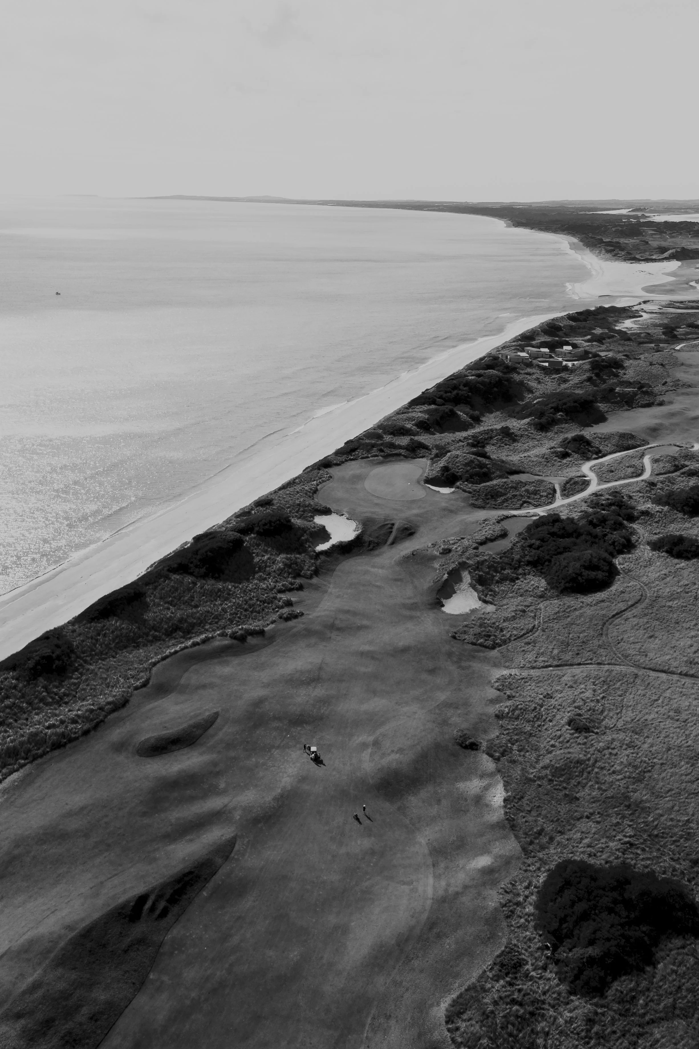 Aerial view of a golf course along a coastline with sandy beaches and water, captured in black and white.