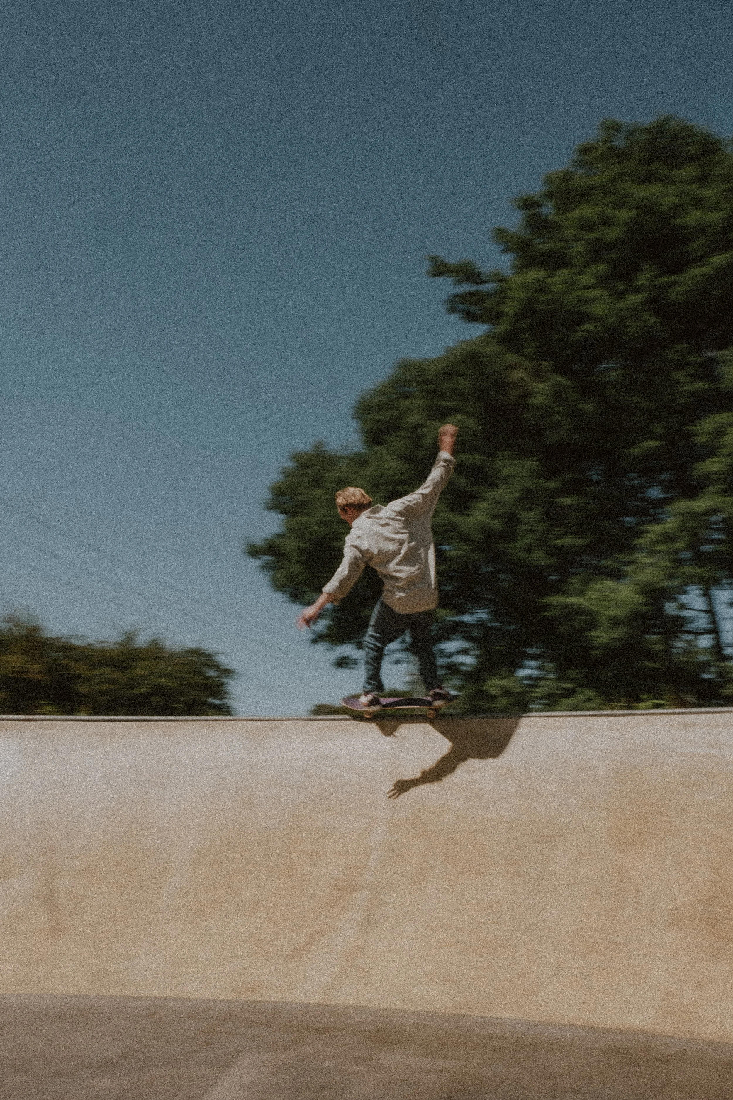 A person skateboarding outdoors on a skateboard, with trees and a clear sky in the background.