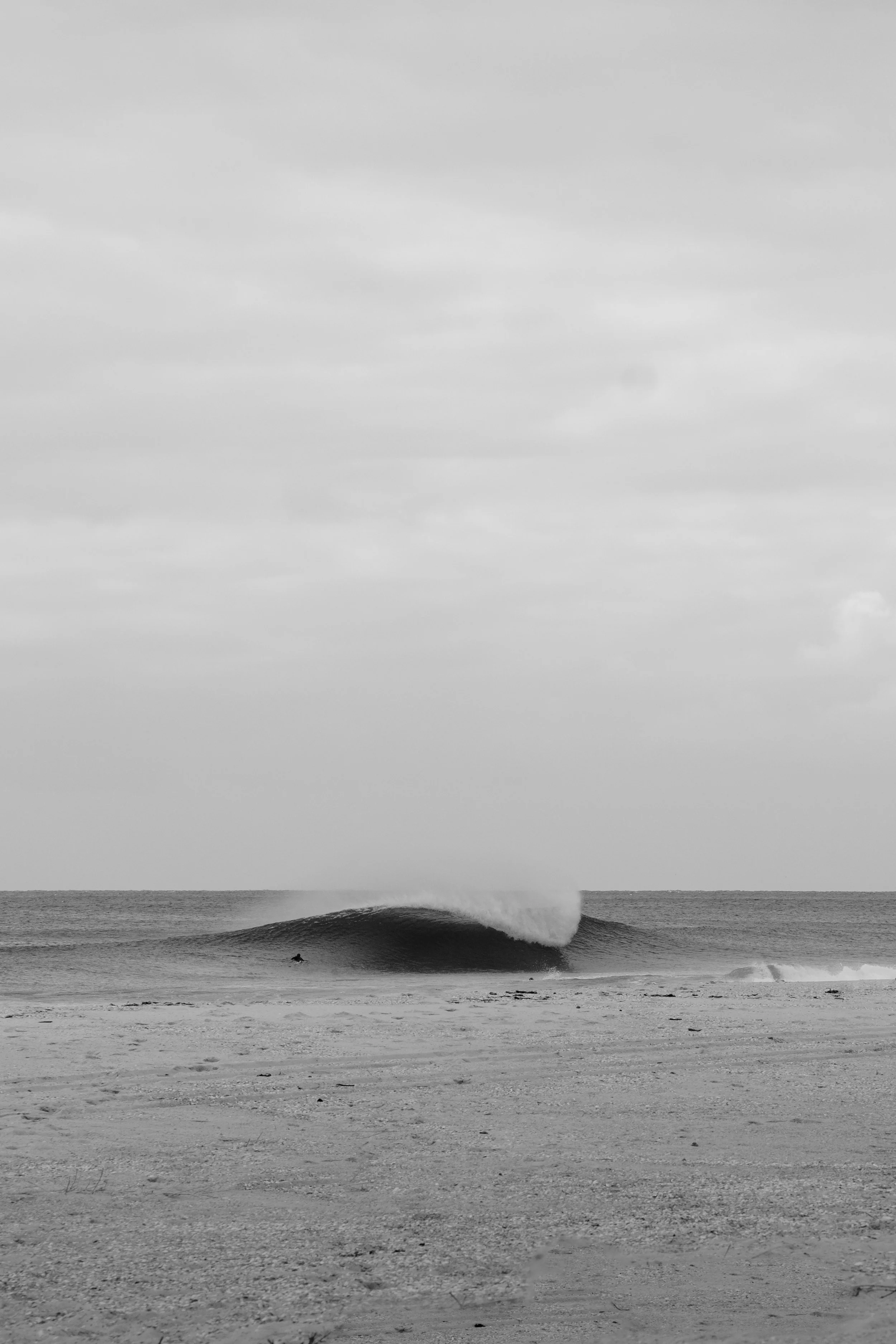 Black and white photo of ocean waves with a surfer on a small wave and overcast sky.
