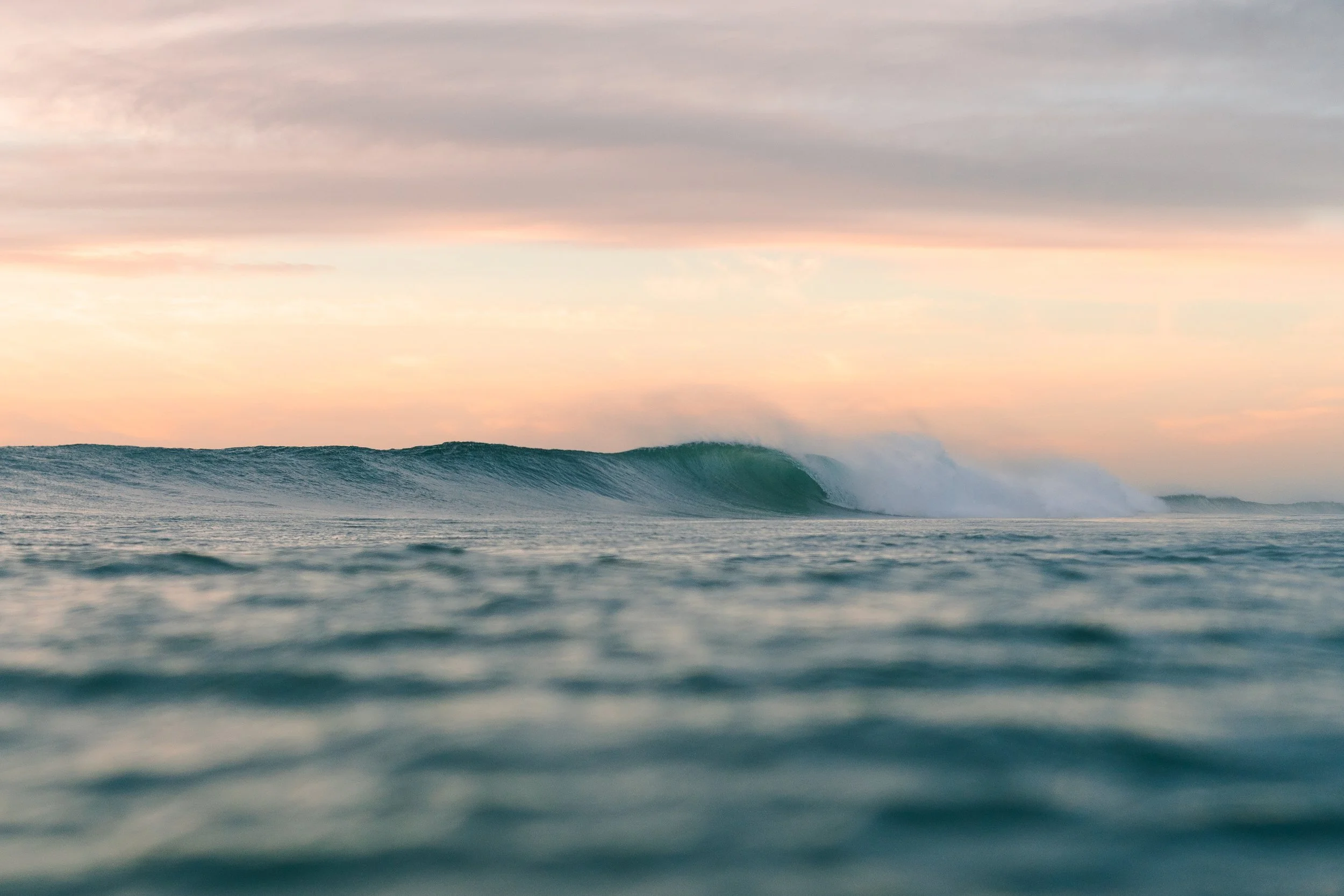 Ocean waves at sunset with a colorful sky.
