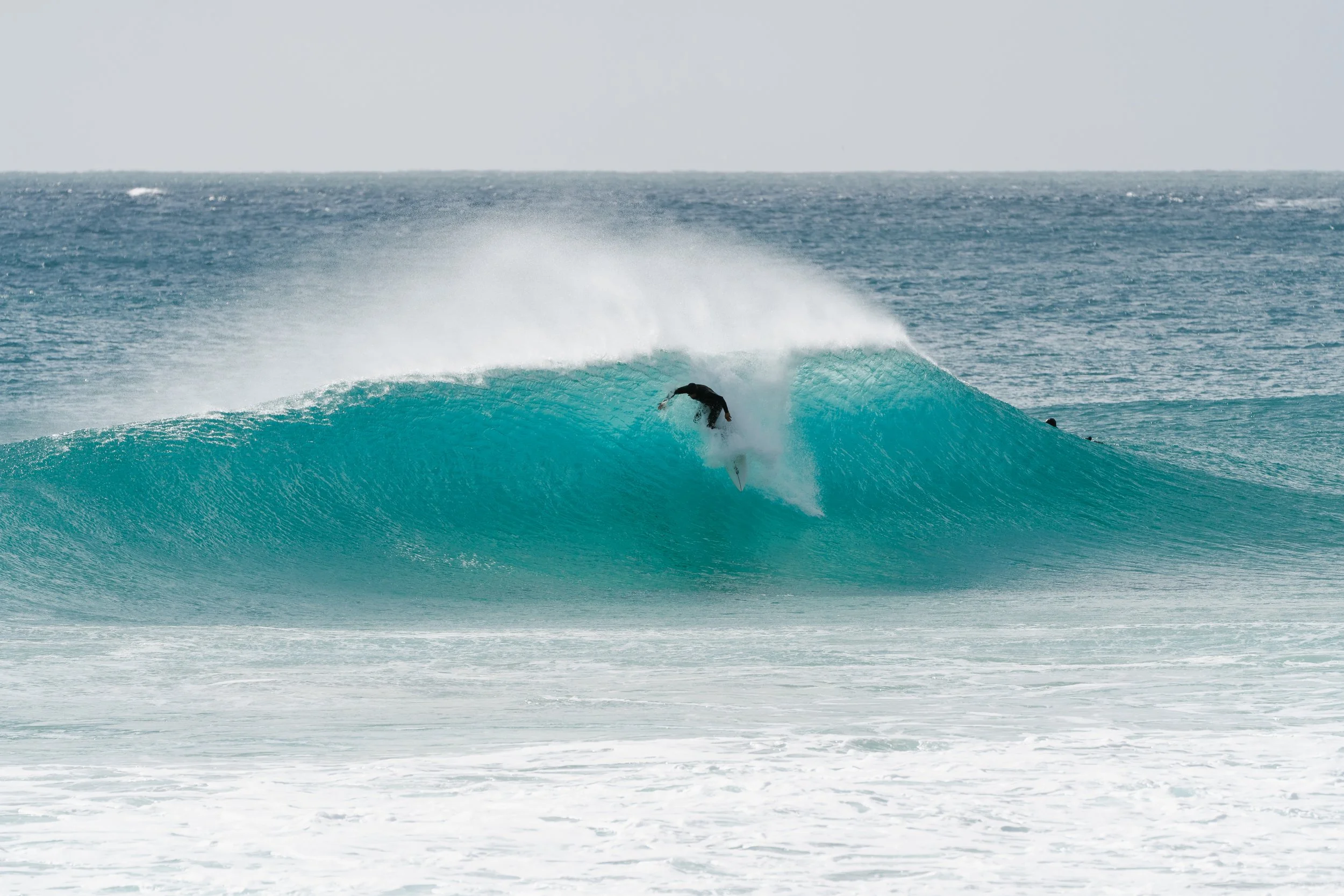 A person is surfing on a turquoise wave at the beach.