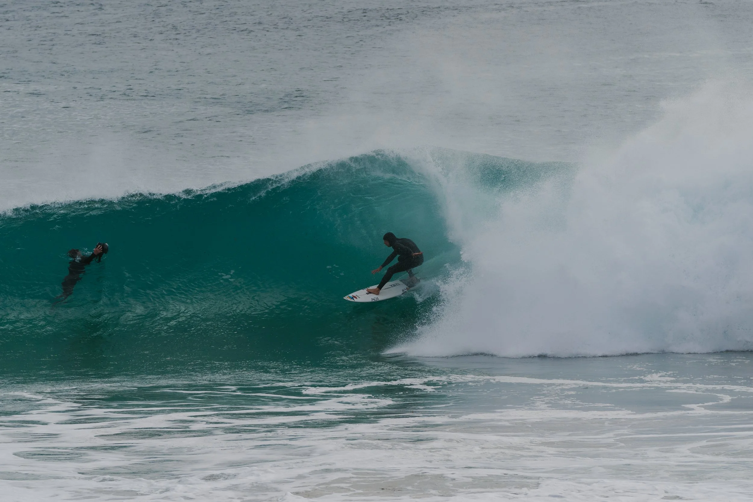 A person riding a surfboard on a wave in the ocean while another person takes a photo in the water.