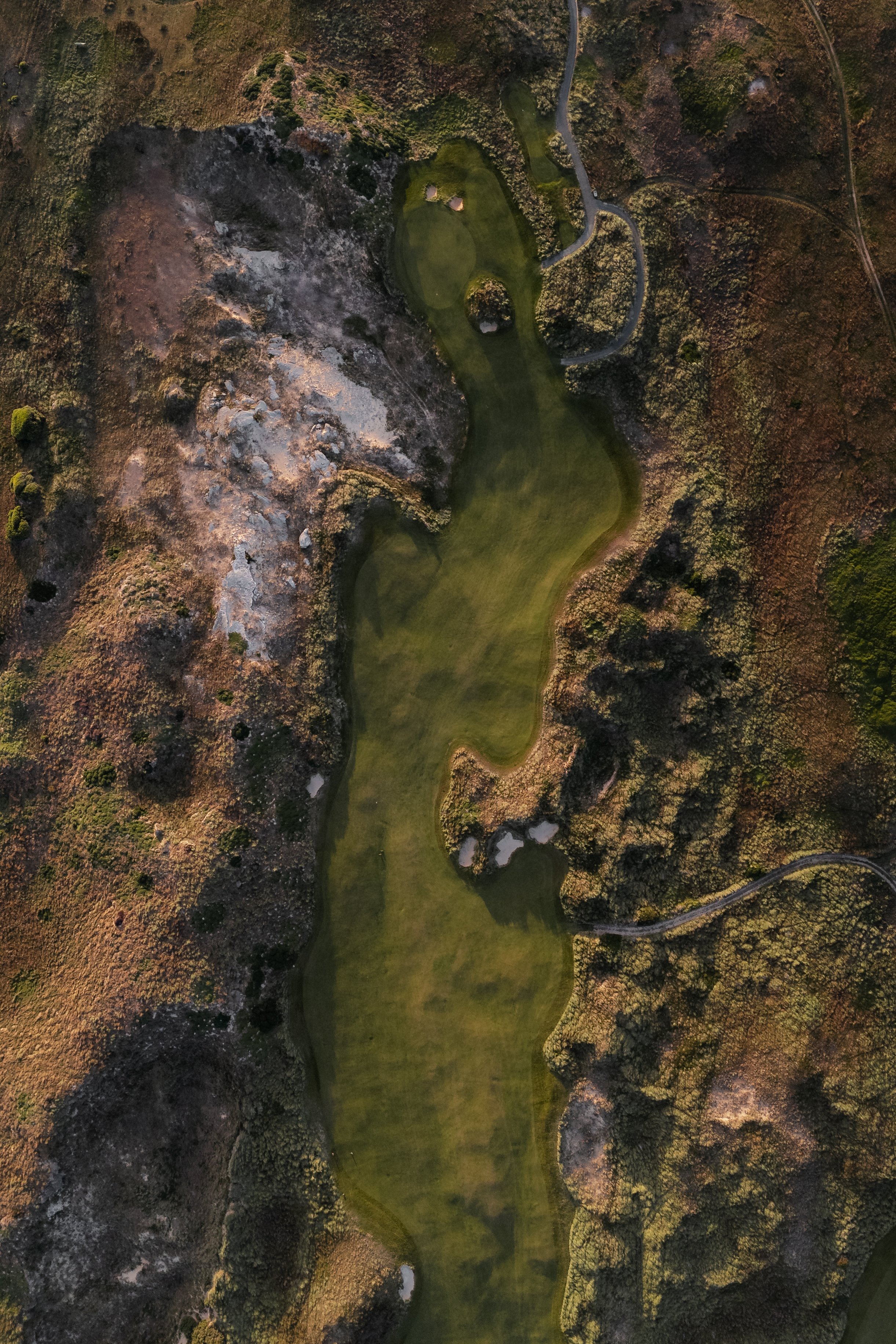 An aerial view of a golf course surrounded by trees and rocky terrain, with fairways and a putting green visible.