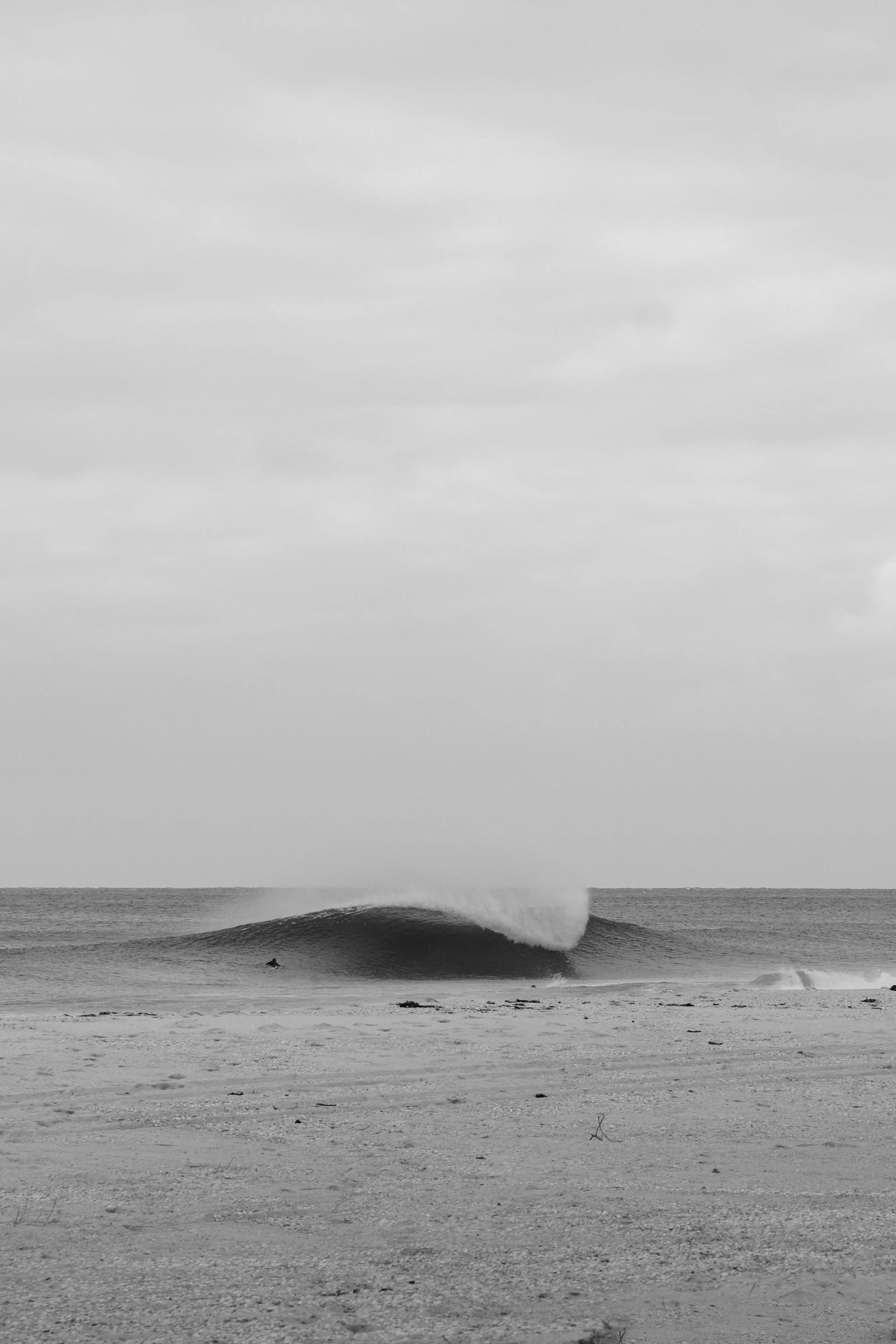 Black and white photo of an ocean wave crashing on the beach, with clouds in the sky.