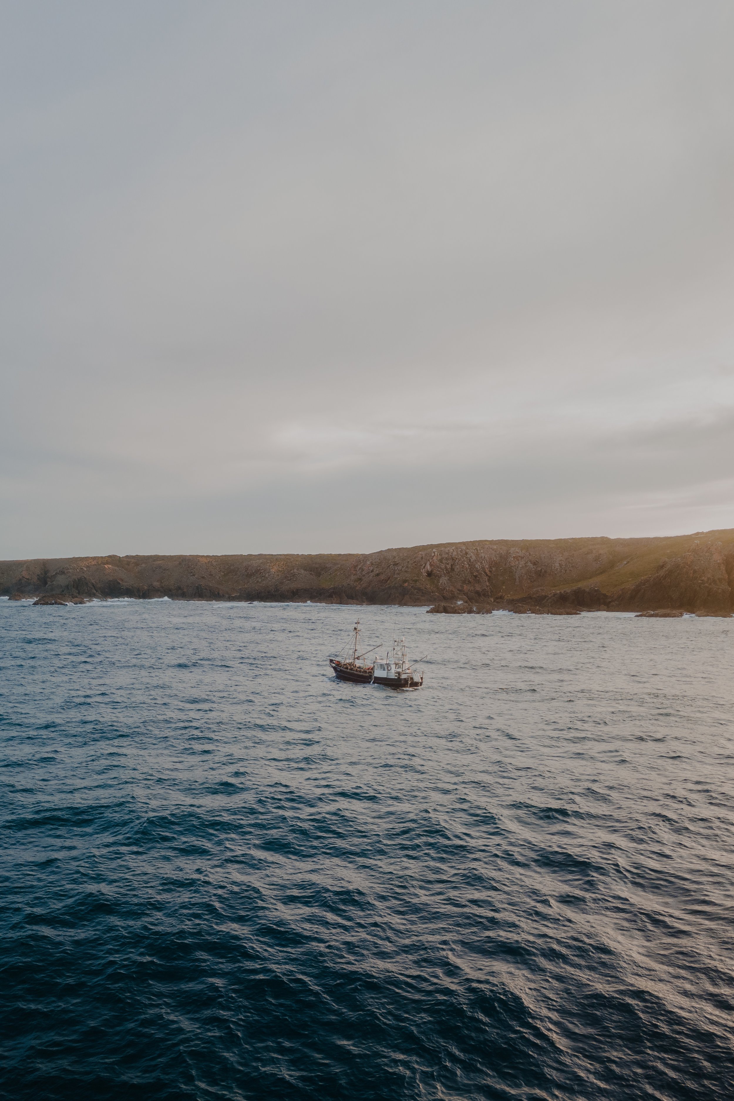 A boat sailing near a rocky coastline under an overcast sky.