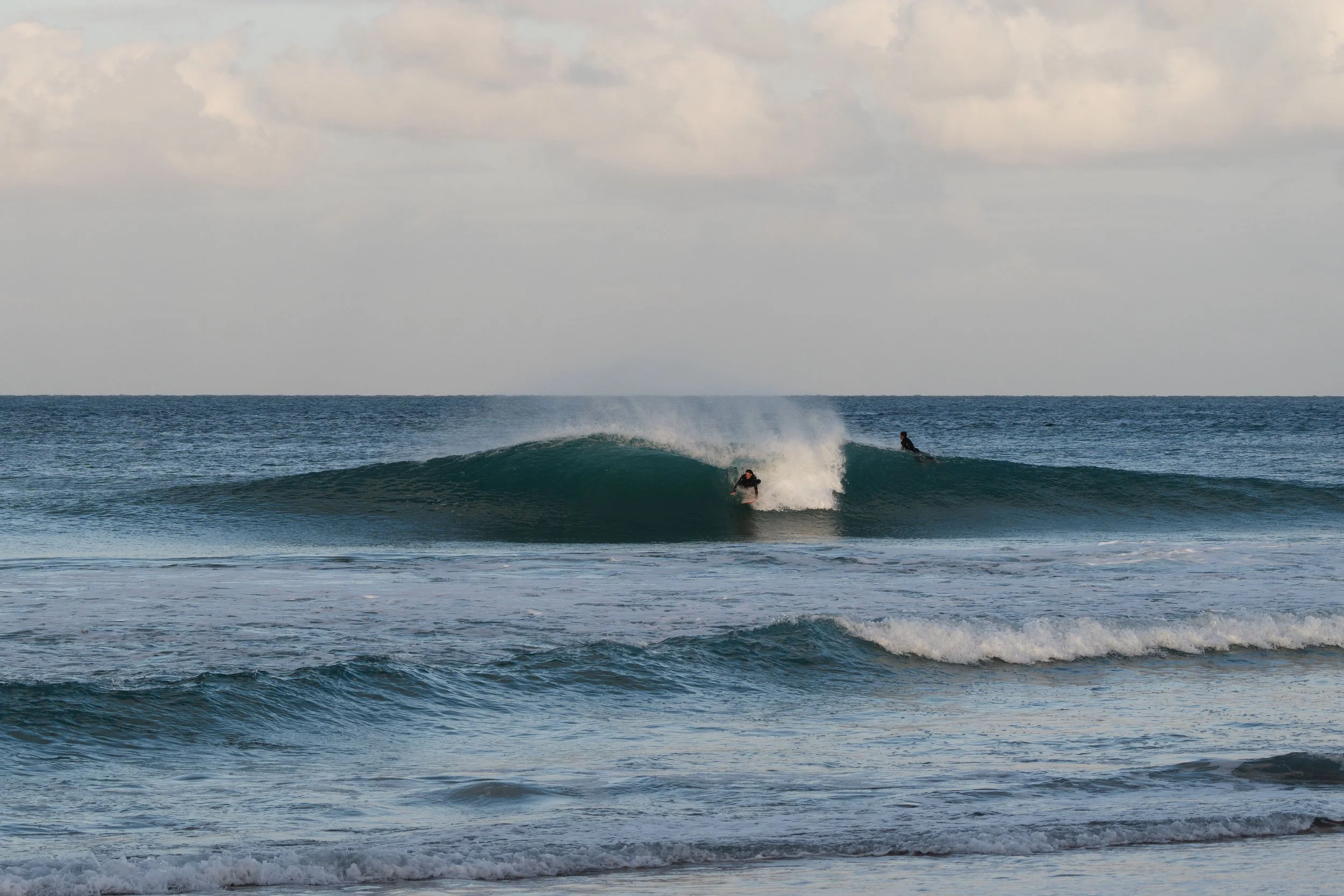 Two surfers riding a wave in the ocean on a cloudy day.