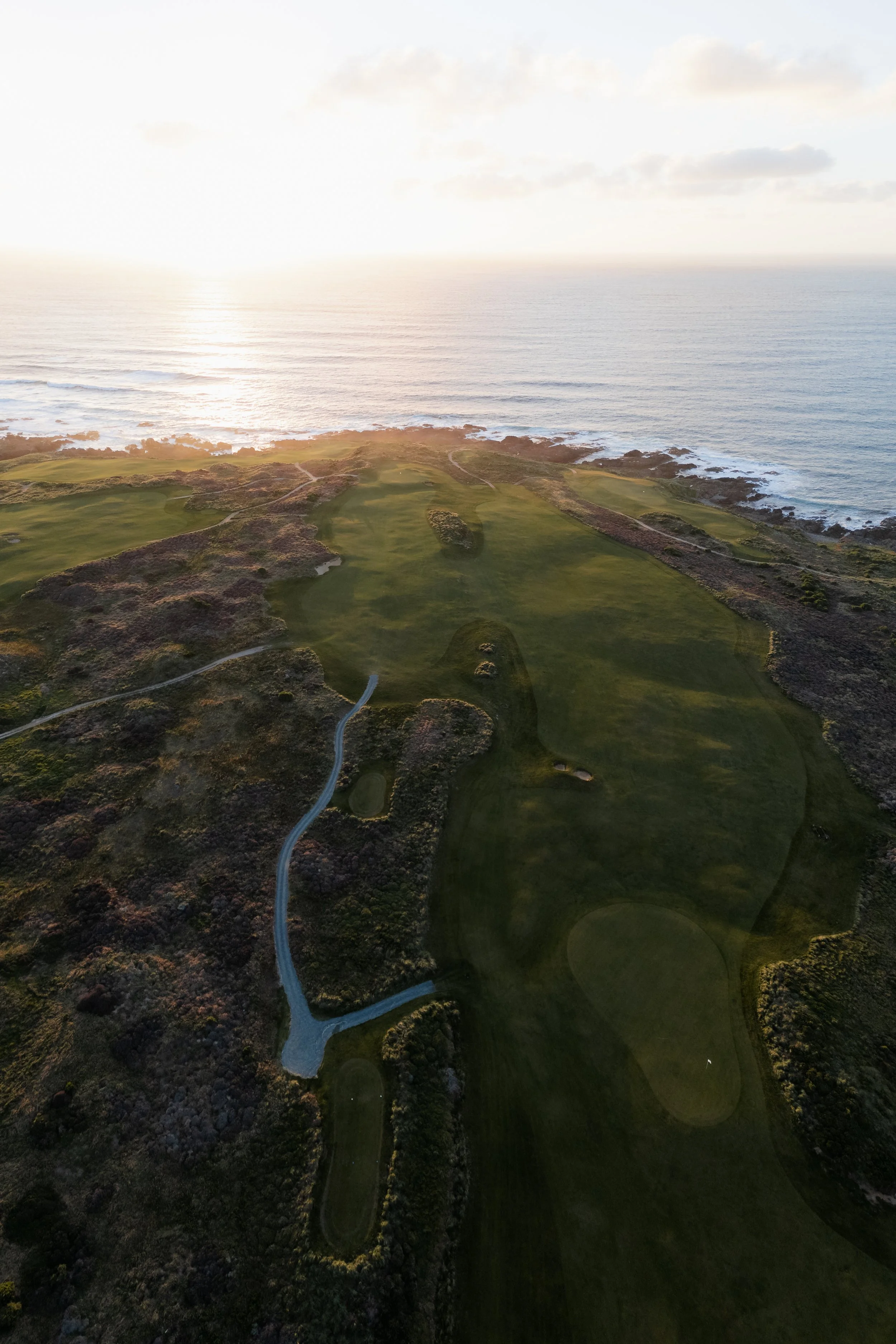 Aerial view of a golf course by the ocean at sunset.