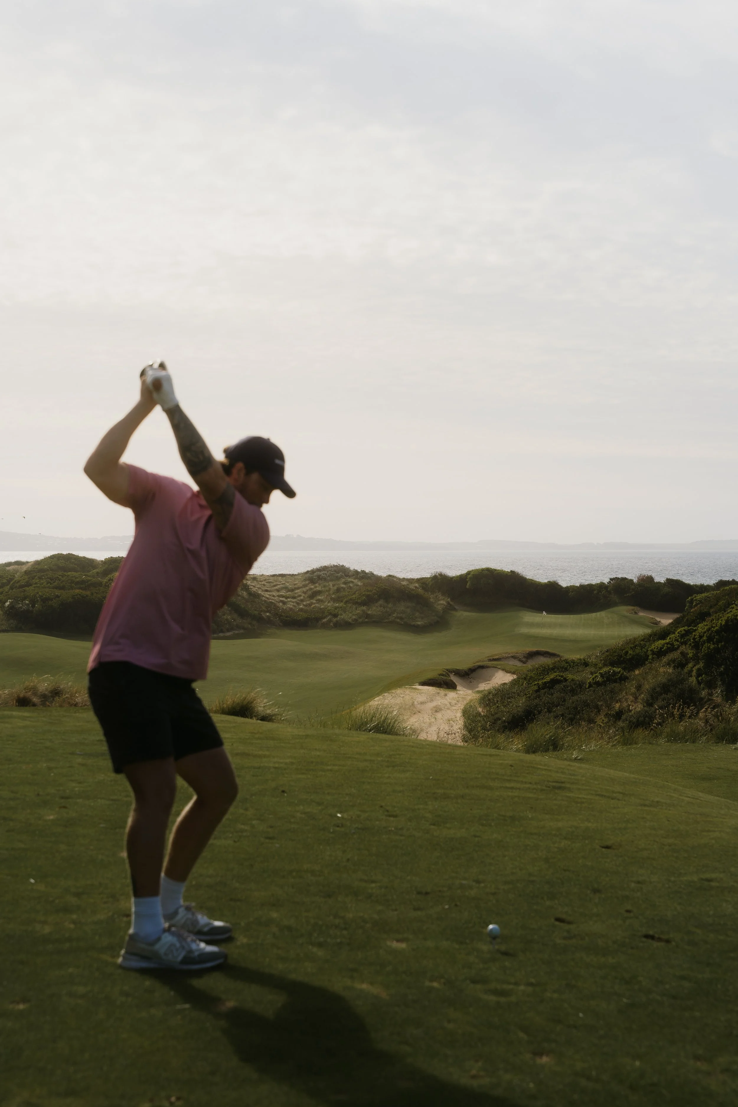 A man playing golf on a course near the water, swinging a golf club to hit a golf ball.