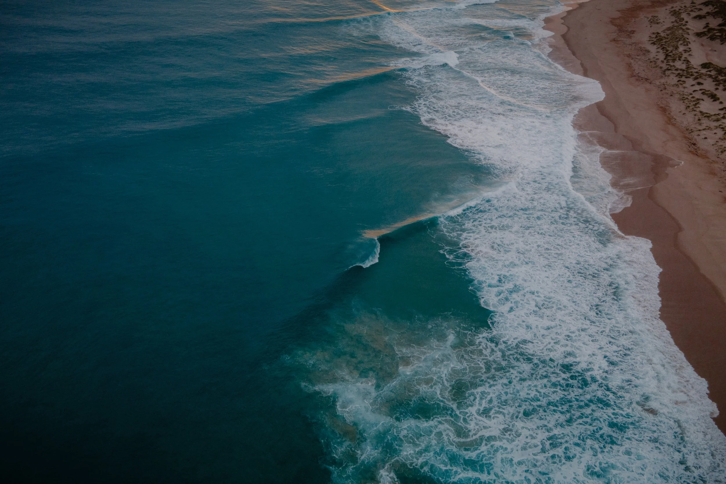 Aerial view of ocean waves crashing onto sandy beach.