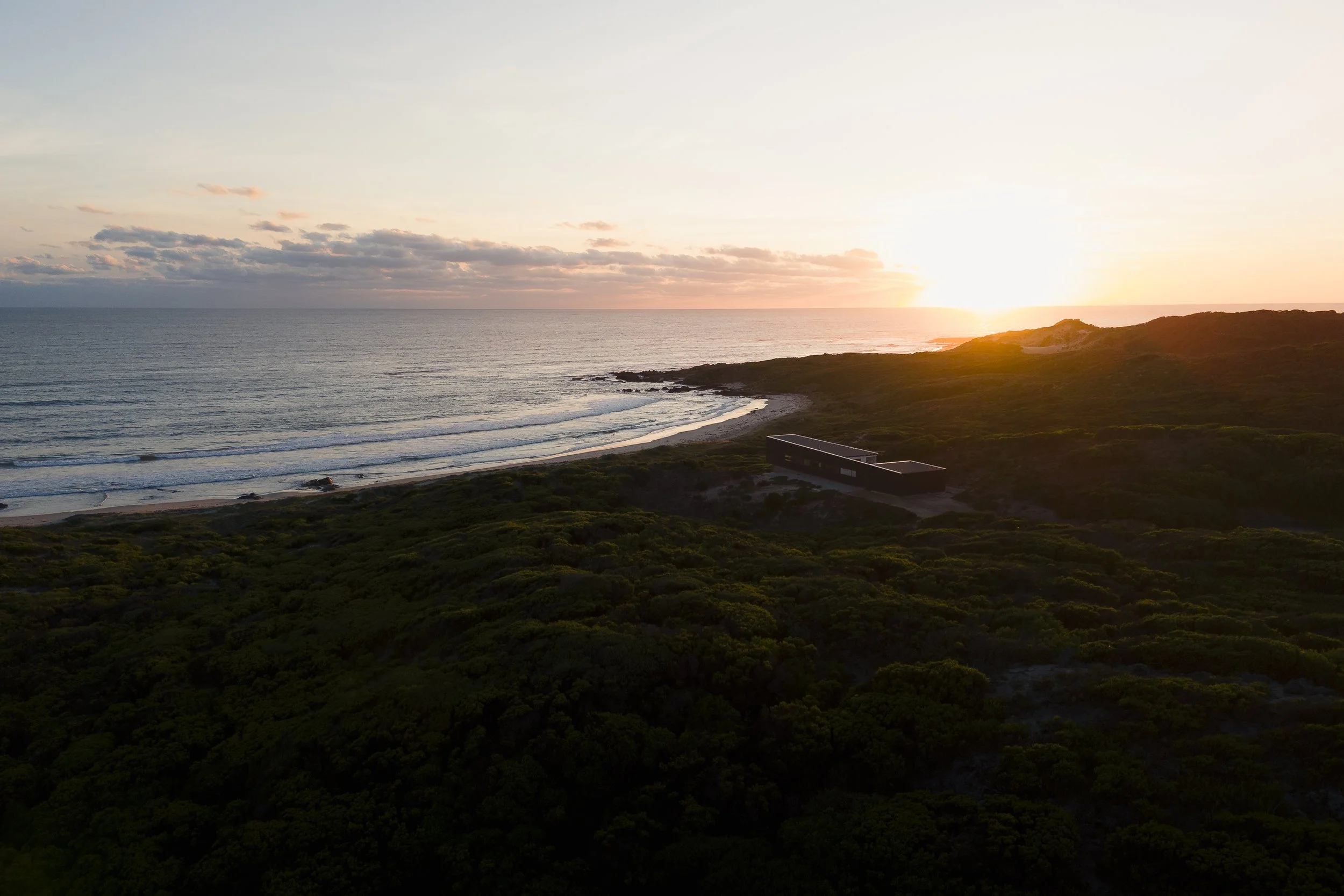 Sunset over the ocean with clouds and a hillside in the foreground.
