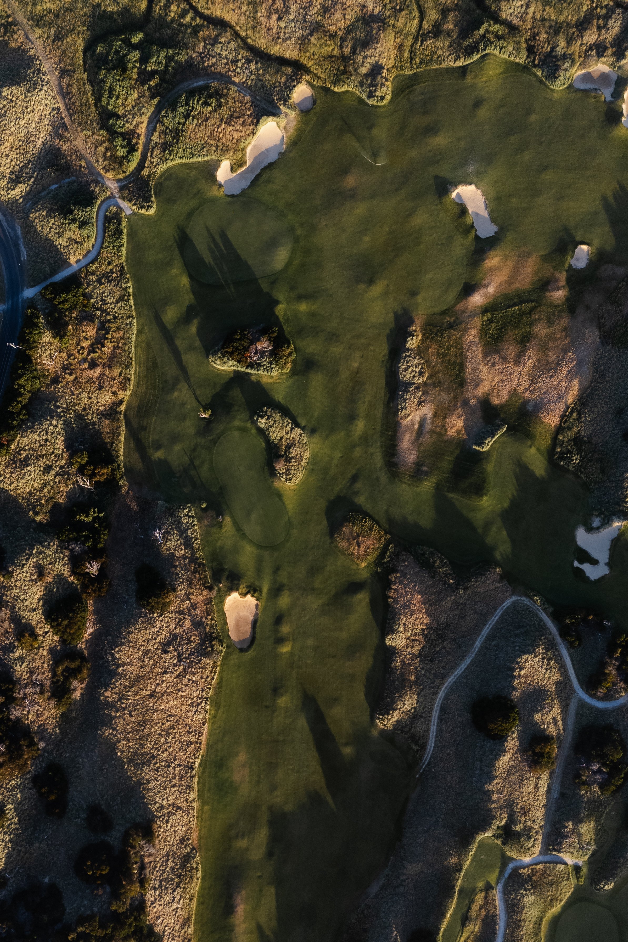An aerial view of a golf course with green fairways, sand traps, water hazards, and surrounding trees.