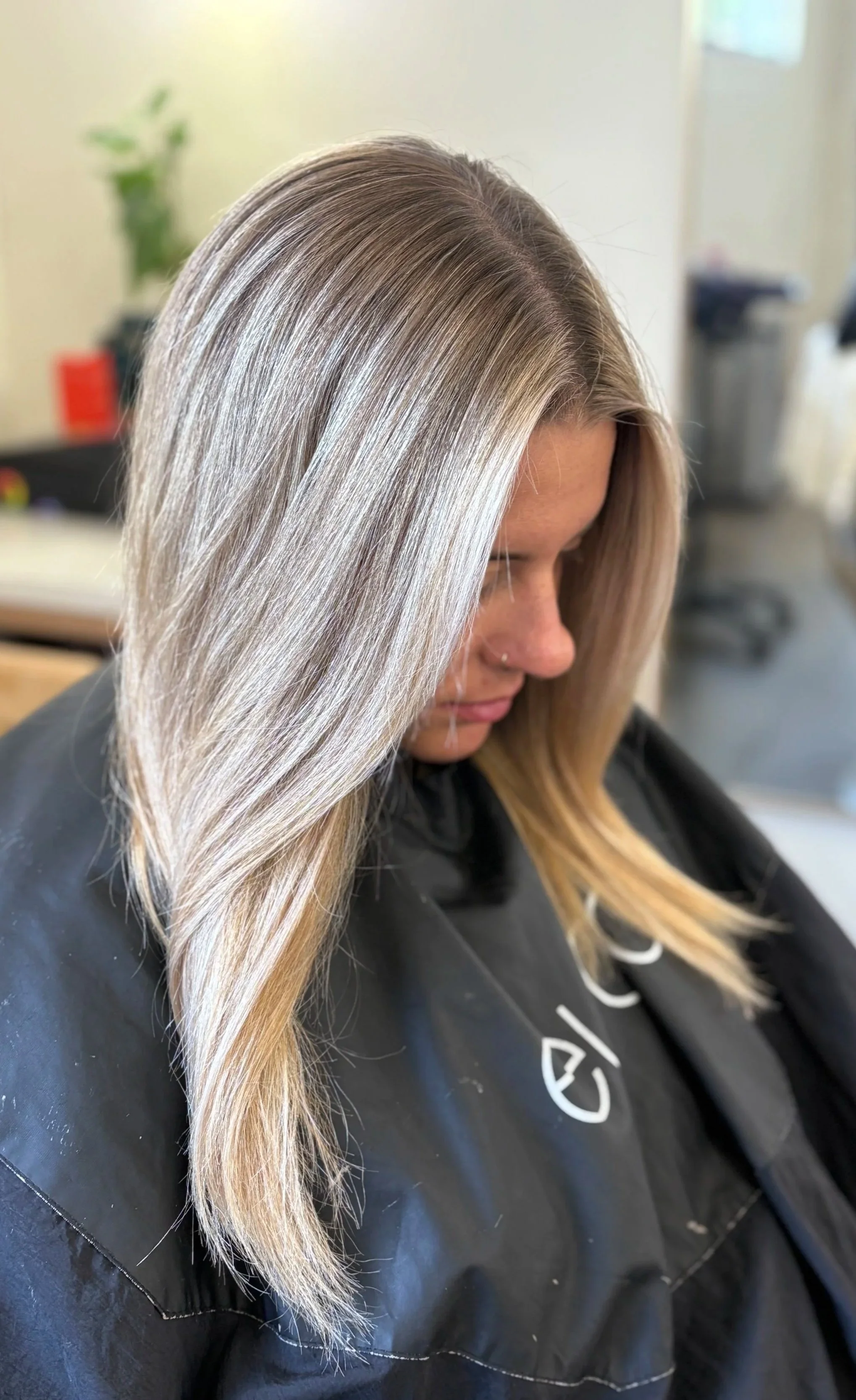 A woman with long, straight, blonde hair sitting in a salon chair, getting her hair styled.