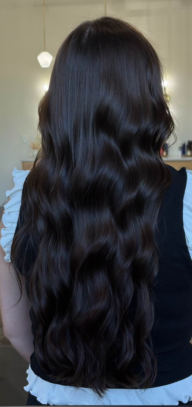 A person with long, dark, wavy hair standing indoors.