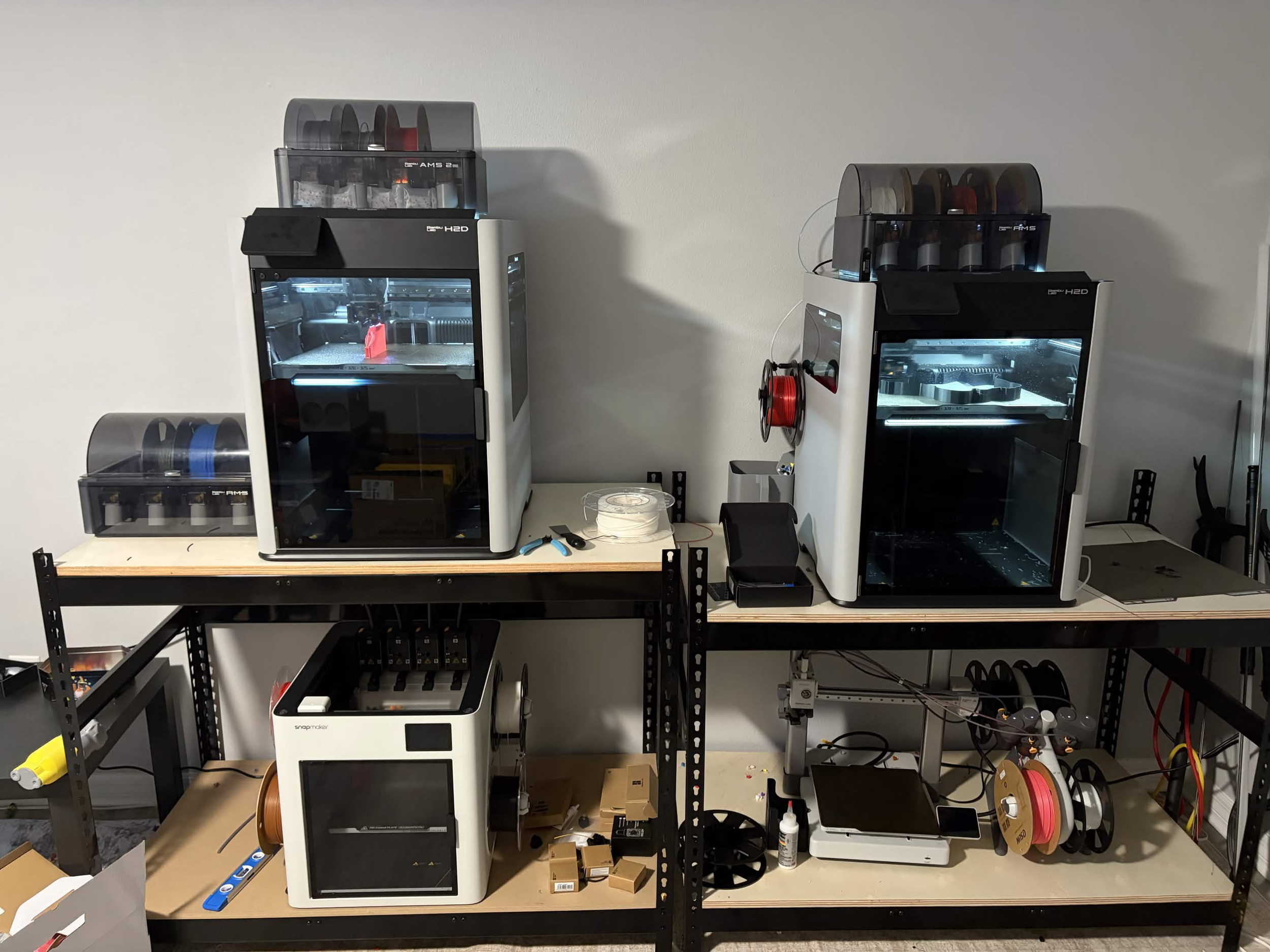 AGDN Prints workspace with 3D printers, filament spools and printing tools on shelves.