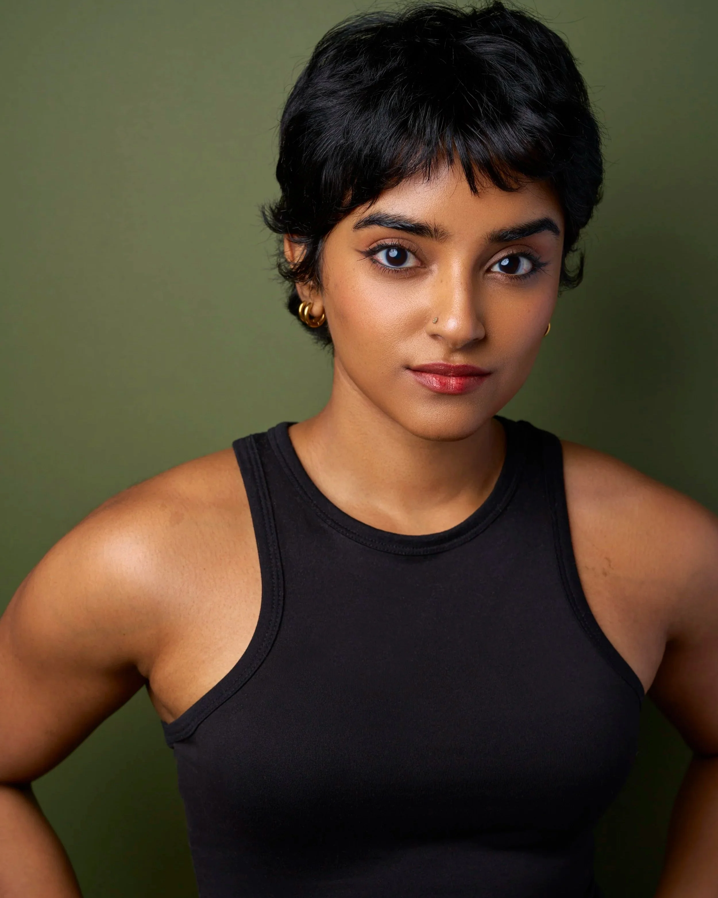 A young woman with short black hair, wearing a black sleeveless top, standing against a green background.