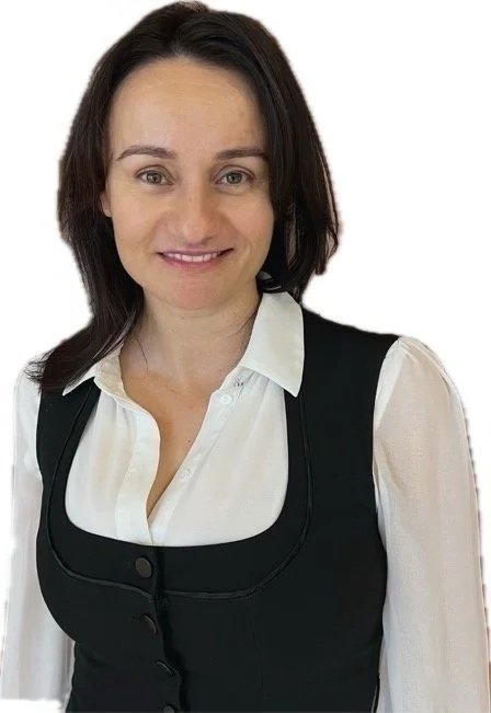 A woman with shoulder-length dark hair, wearing a white blouse and black vest, smiling at the camera against a white background.
