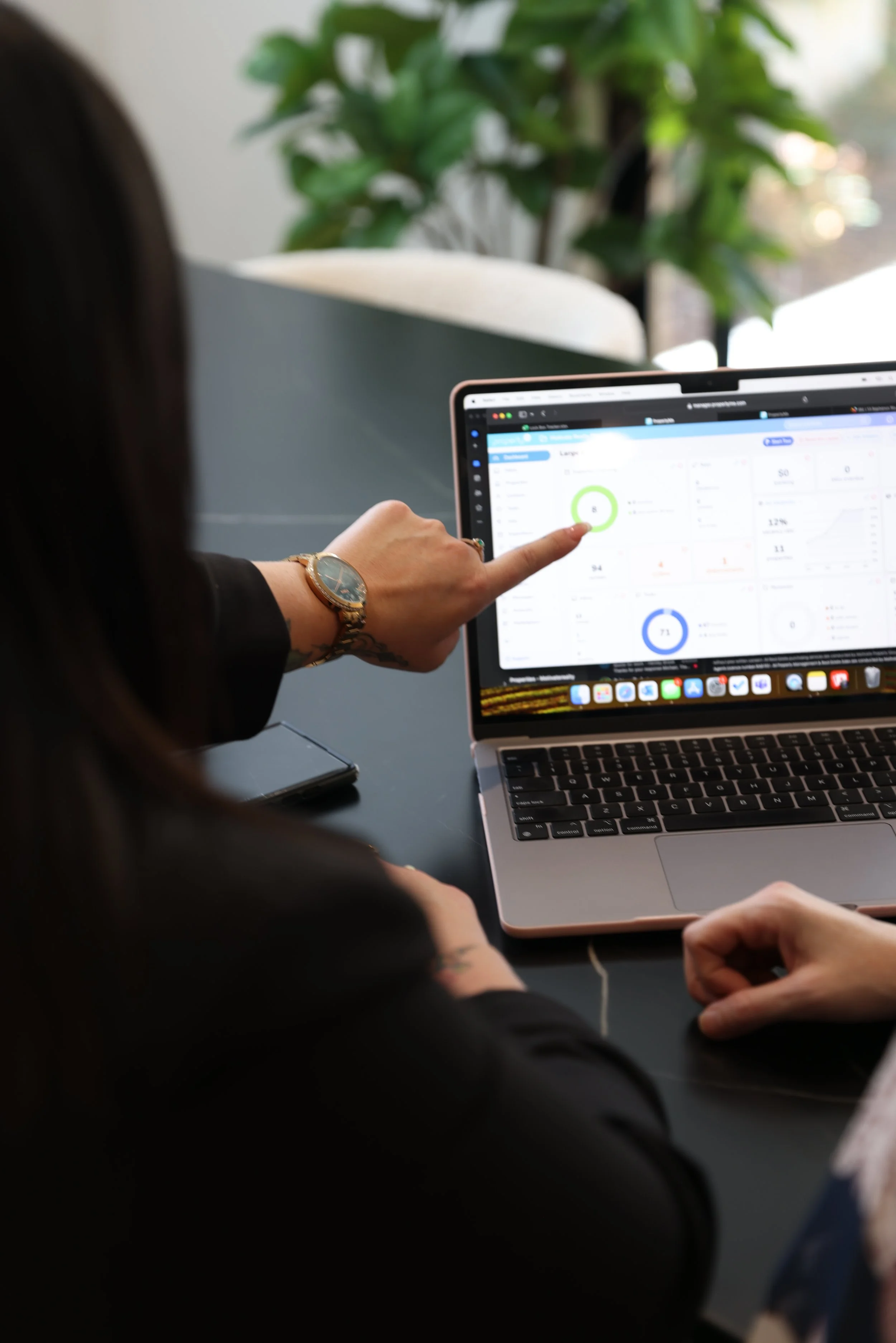 Person using a laptop displaying a dashboard with graphs and metrics, pointing at the screen during a workspace setting.