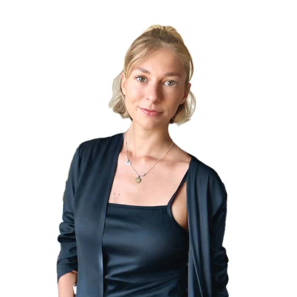 A young woman with blonde hair, wearing a black tank top and a matching black jacket, smiling softly against a white background.