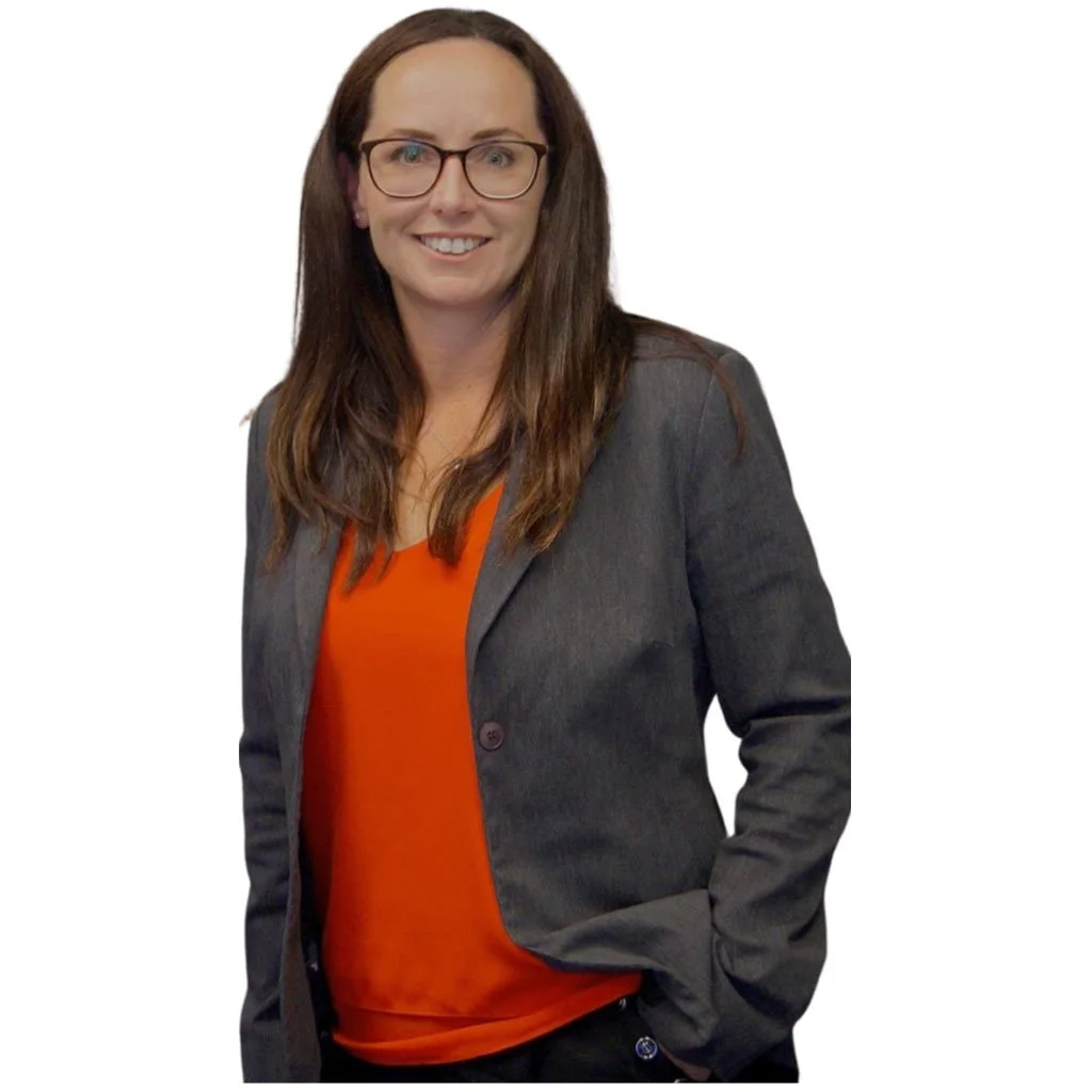 A woman with long brown hair wearing glasses, a dark gray blazer, and an orange top, smiling and standing against a white background.