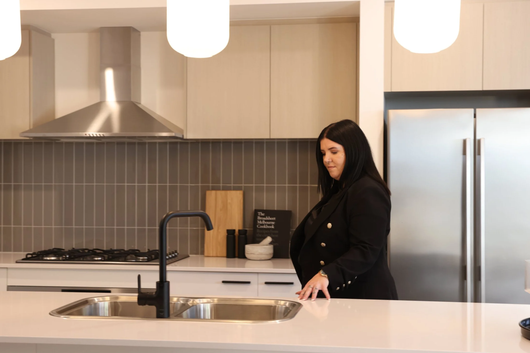 Woman with dark hair standing at a kitchen island in a modern kitchen, looking down at the surface.