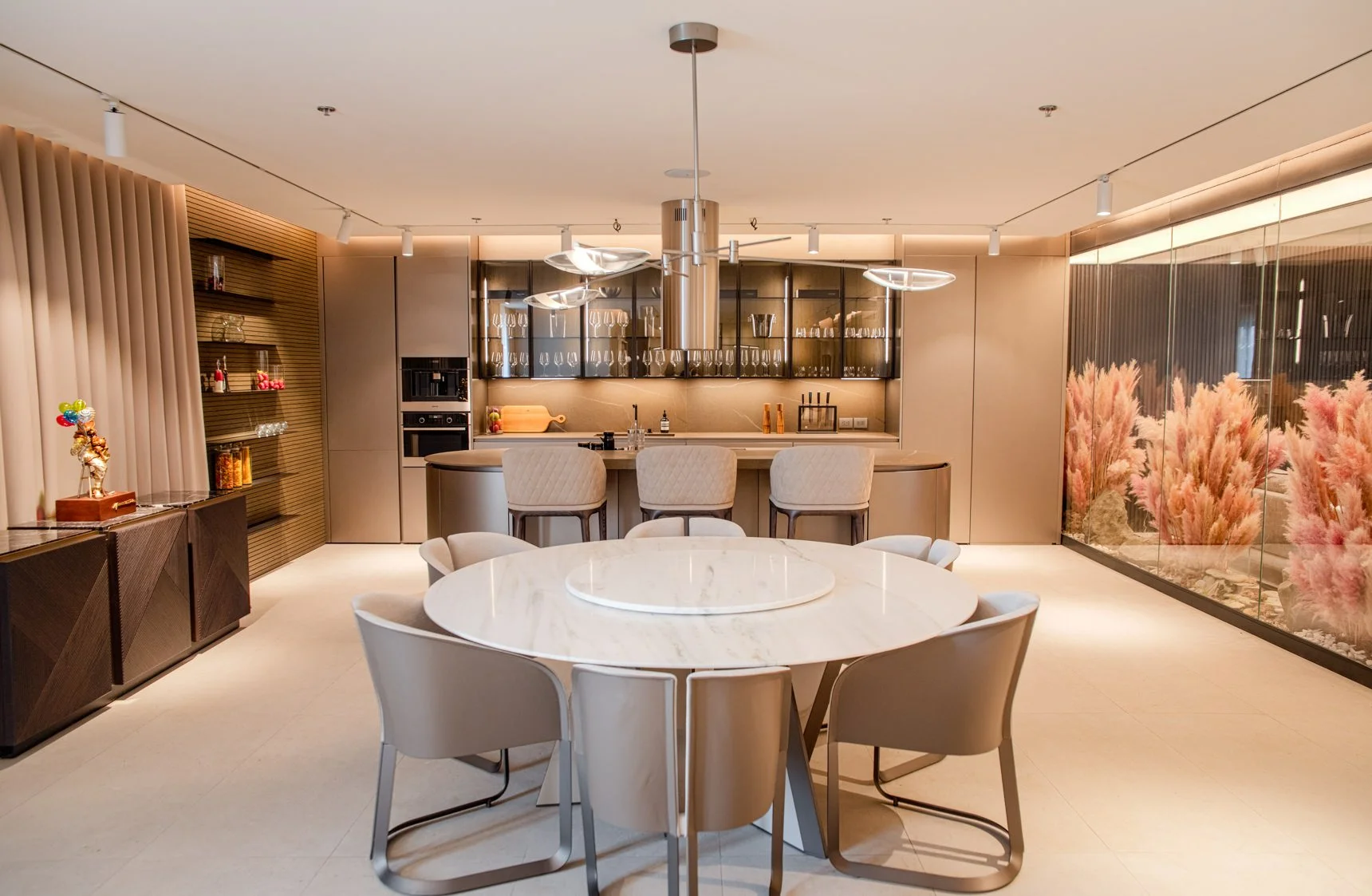 Modern kitchen and dining area with round marble table, beige chairs, bar counter, and decorative plants