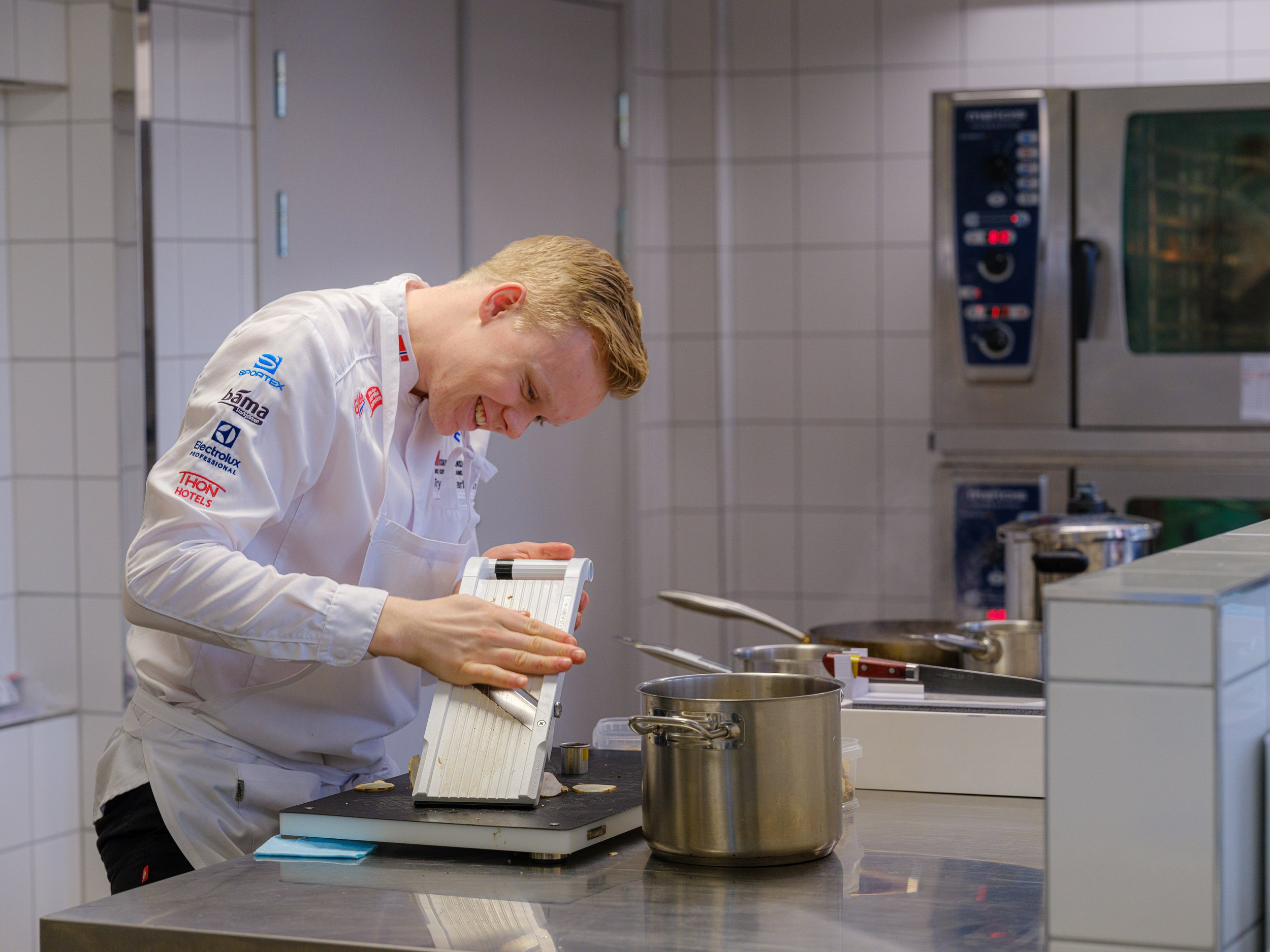 Person i kokkeuniform som skiver en rett i et kjøkken.