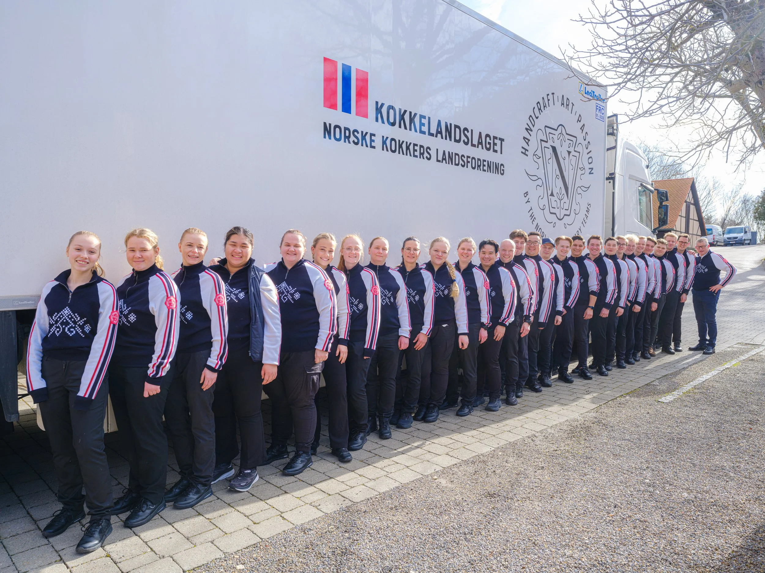 En gruppe unge kvinner og menn står sammen ved siden av en stor lastebil med logoen til Norsk Kokker Landsforening.