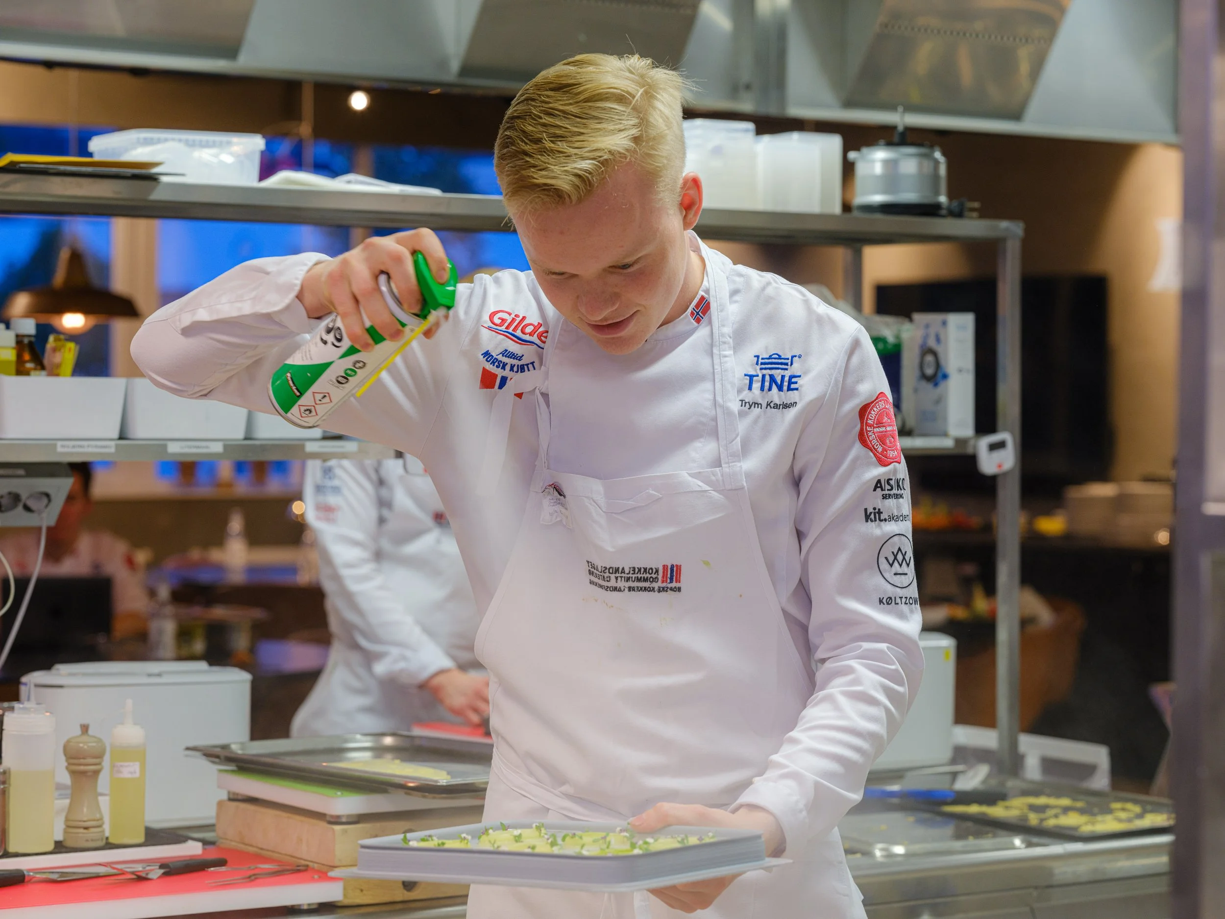 Kokk som sprayer olje på en tallerken i et kjøkken.