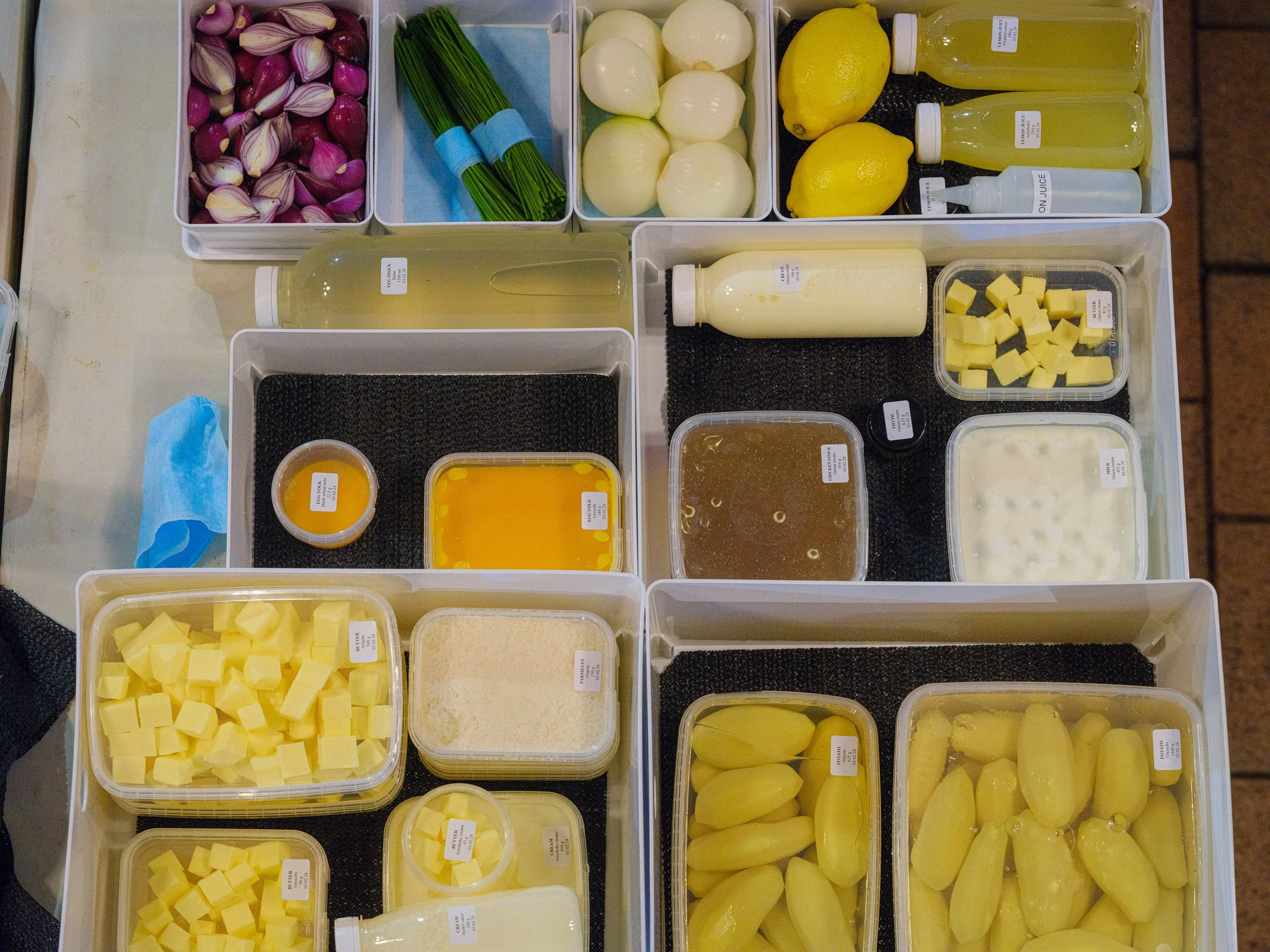 En oversikt over ulike typer mat, inkludert løk, grønne urter, sitroner, sauser, ost, og andre ingredienser i plastbeholdere og flasker.