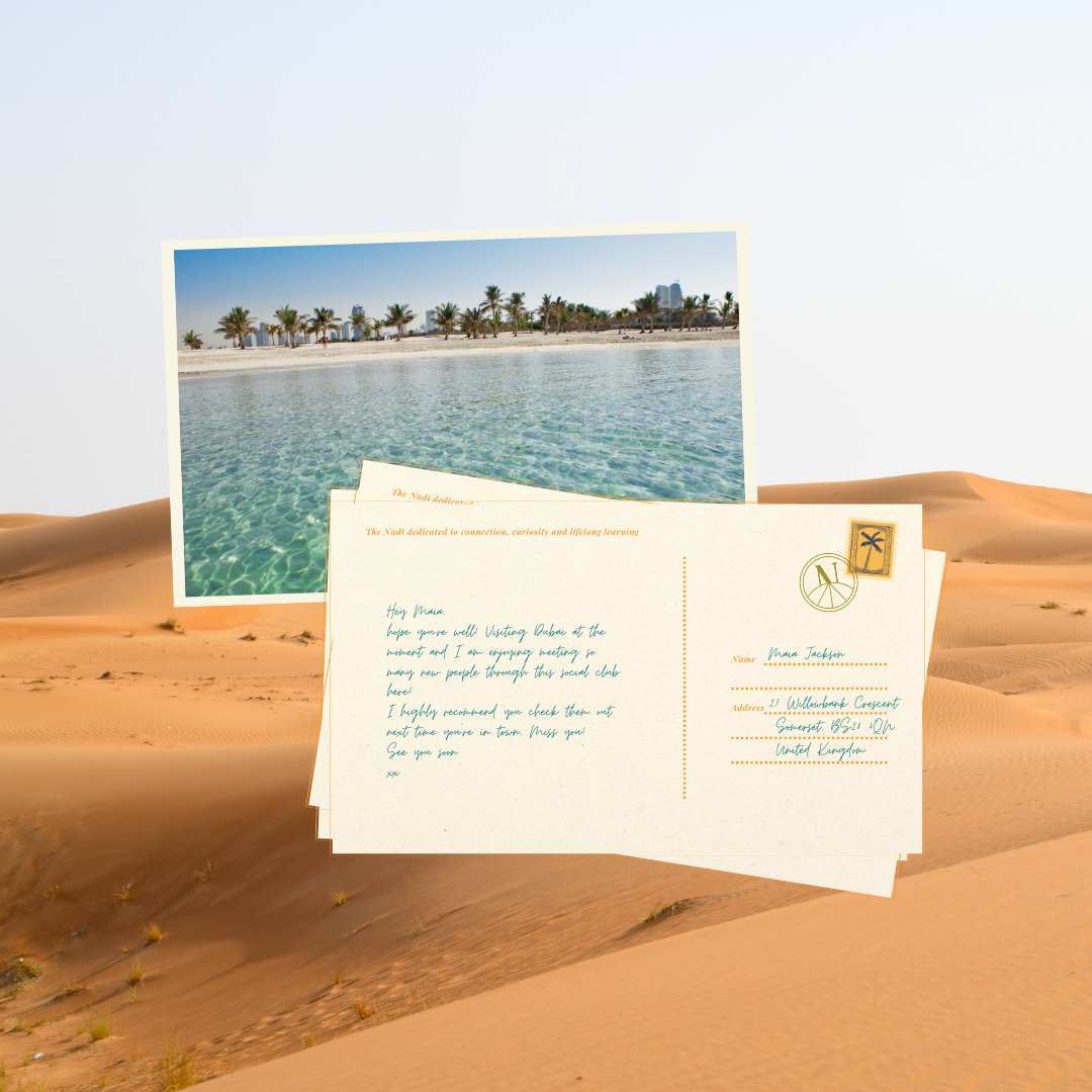 A postcard in the desert with a Dubai beach scene photograph and a handwritten letter, surrounded by sand dunes.