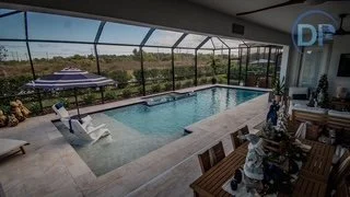 Indoor pool area with a screened enclosure, poolside lounge chairs, a dining table with chairs, and outdoor scenery in the background.