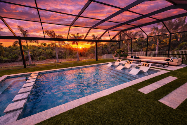 Covered outdoor pool area with lounge chairs at sunset, surrounded by palm trees and greenery.