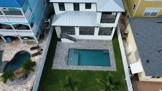 A backyard with a rectangular swimming pool, surrounded by a grassy lawn and a stone patio.